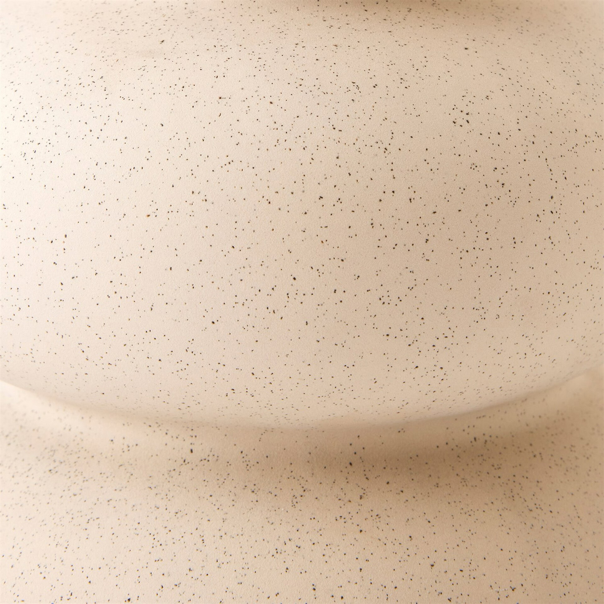 Close-up of a light beige, speckled texture with small dark brown dots, featuring a subtle horizontal curve.
