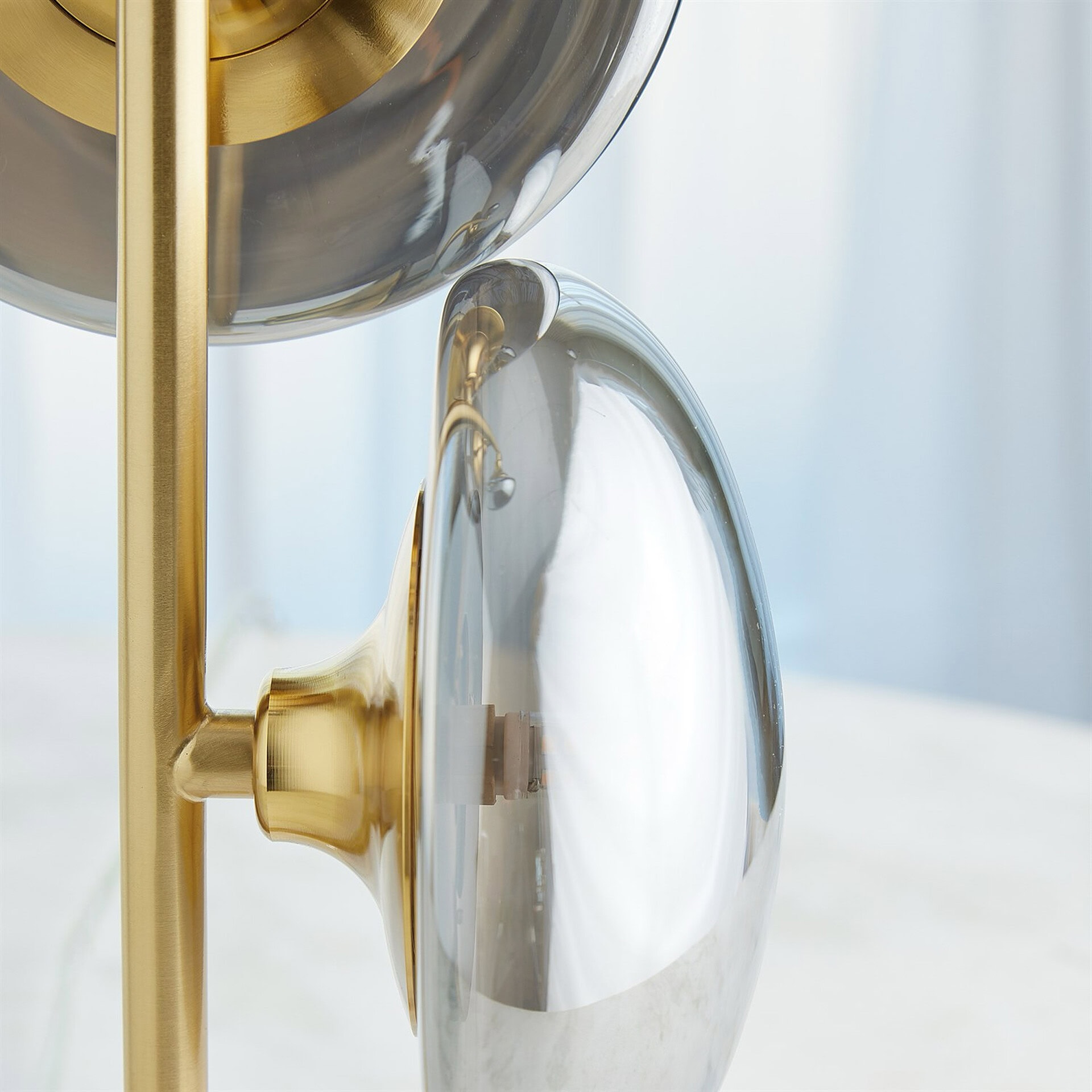 Close-up of a modern light fixture featuring a polished brass rod and fittings, holding clear, elongated glass elements against a soft, light background.