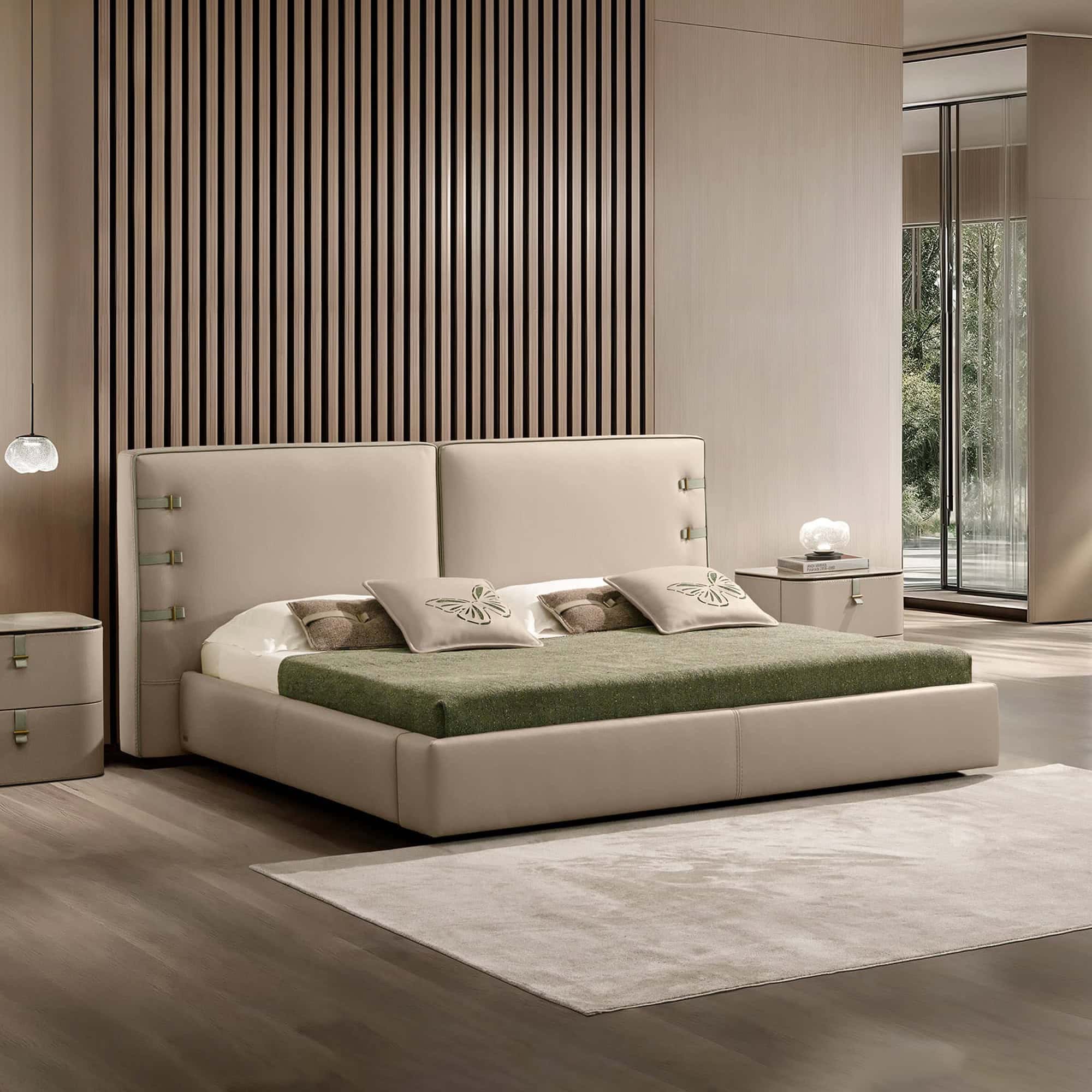 A modern bedroom with a beige upholstered bed, green blanket, and butterfly pillows. A slatted wooden accent wall is behind the bed, and a large window shows green trees. Beige nightstands with lamps flank the bed.