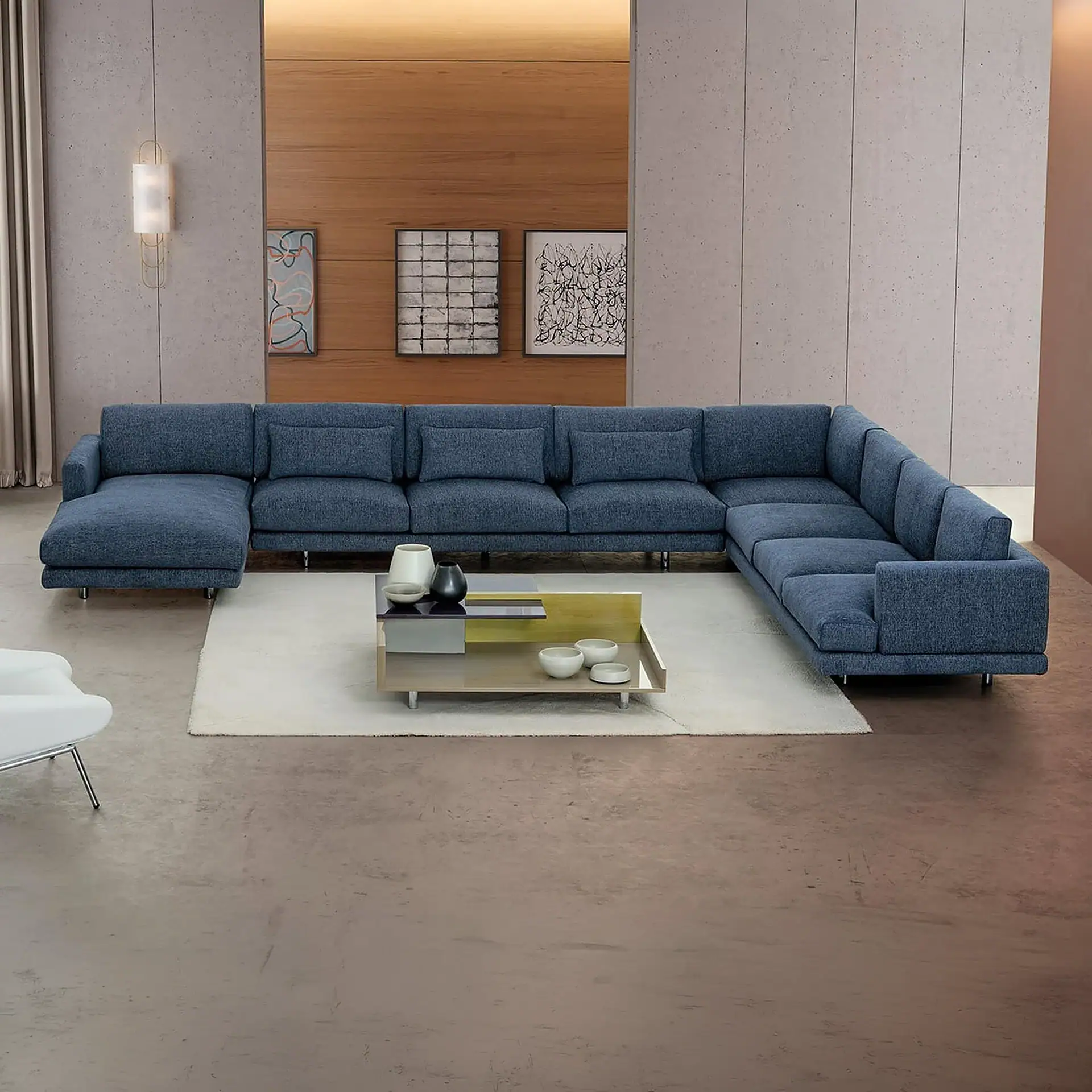 A modern living room with a large U-shaped blue sectional sofa, a multi-level coffee table, and abstract art on the walls.