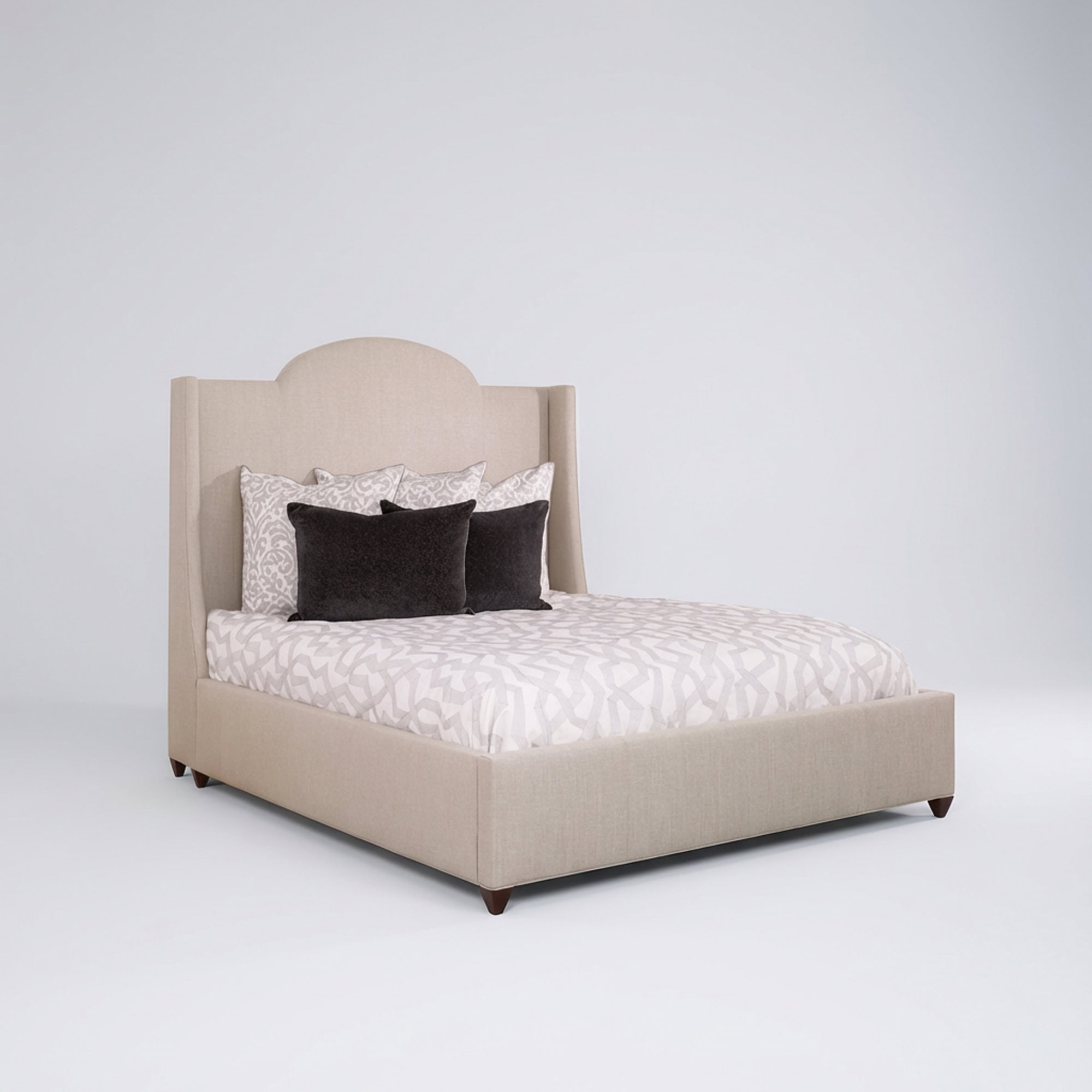 A modern upholstered bed with an arched headboard and wingback sides, in a light beige fabric. The bed is dressed with white and light grey geometric patterned bedding, and two grey patterned pillows with two solid dark grey pillows.
