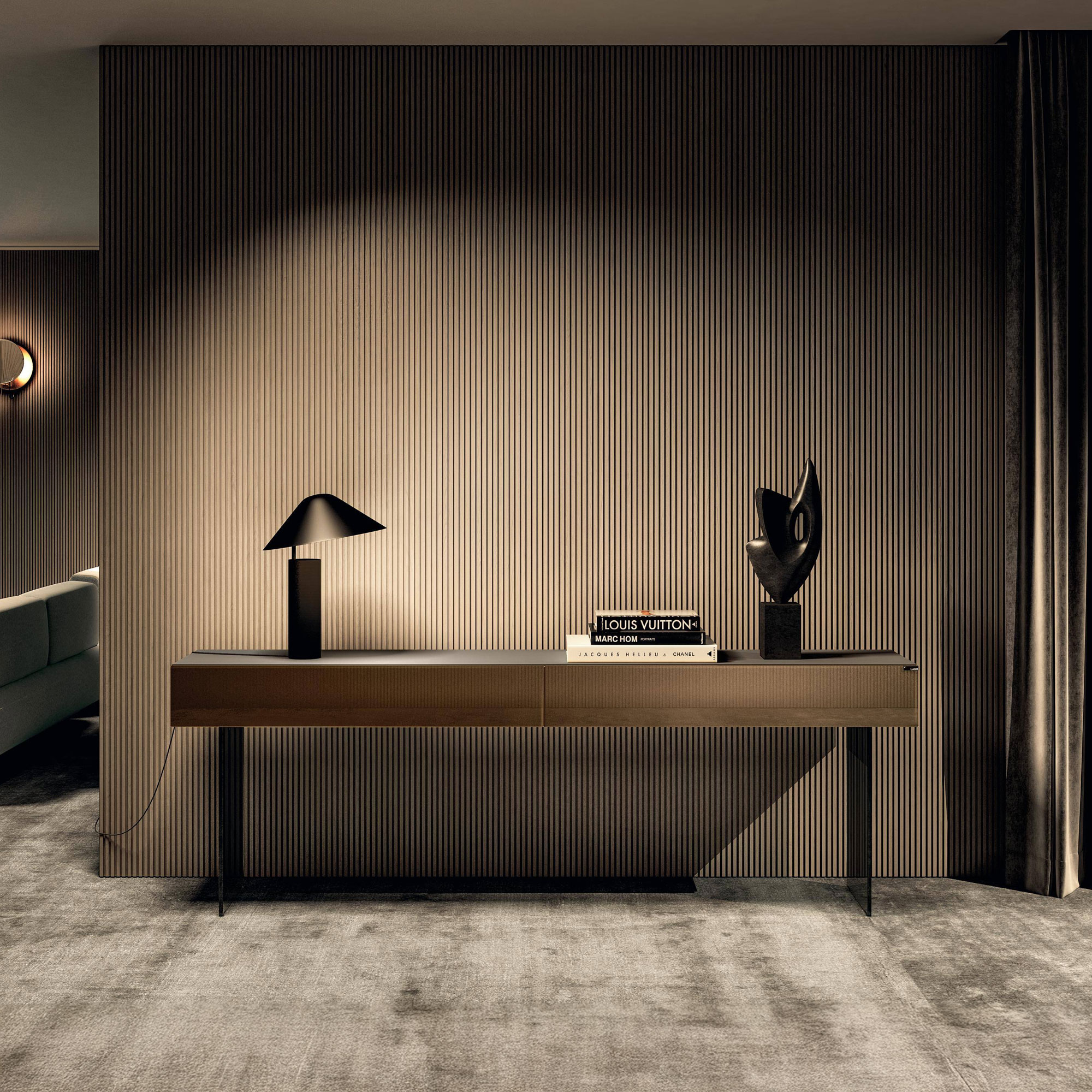 A modern console table with a black lamp, designer books, and an abstract sculpture, set against a dark, vertically fluted wall in a dimly lit, sophisticated room with a grey carpet.
