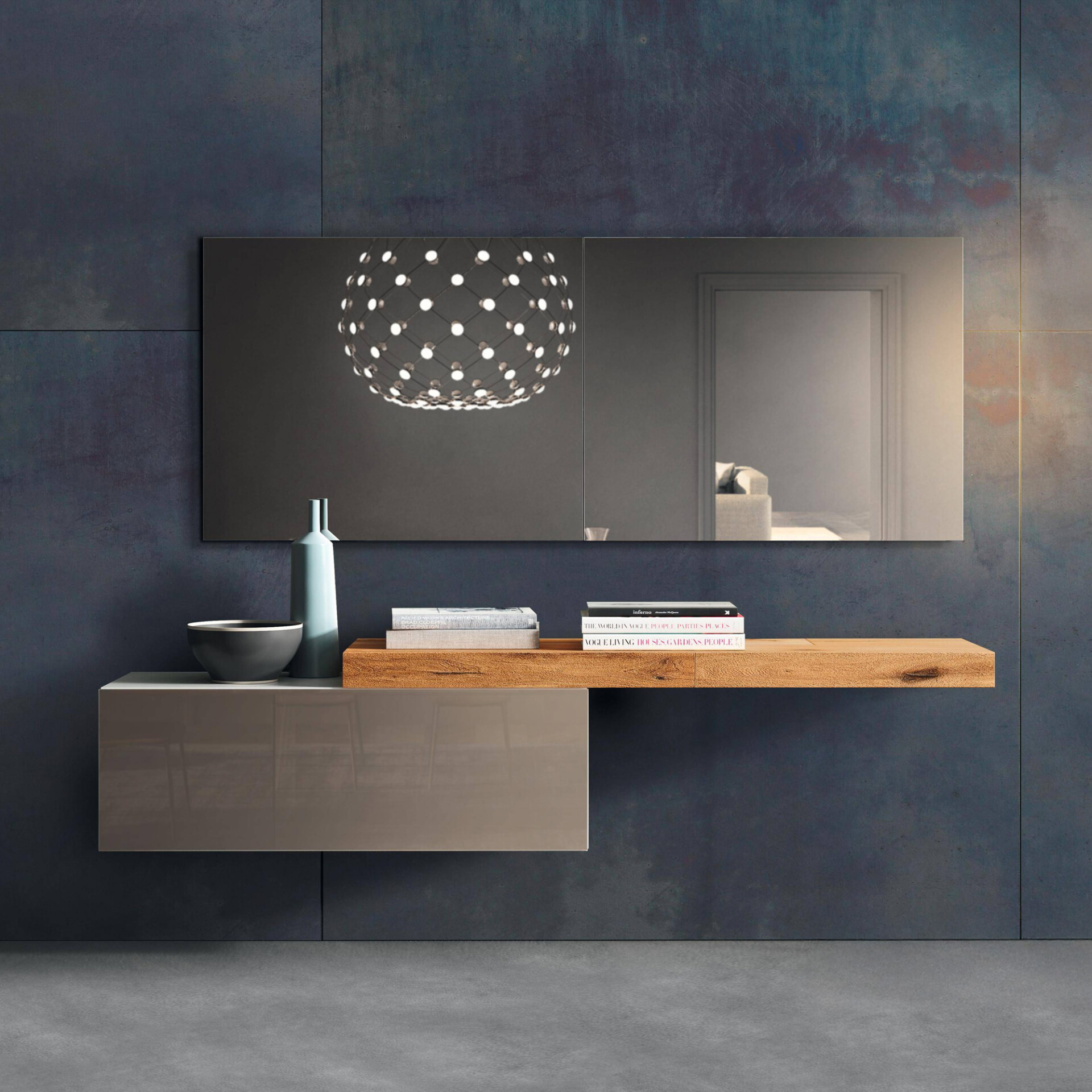 A modern floating console with a glossy taupe cabinet and a rustic wooden shelf, adorned with a vase, bowl, and books, set against a dark, textured wall. A large mirror above reflects a spherical chandelier and a distant room.