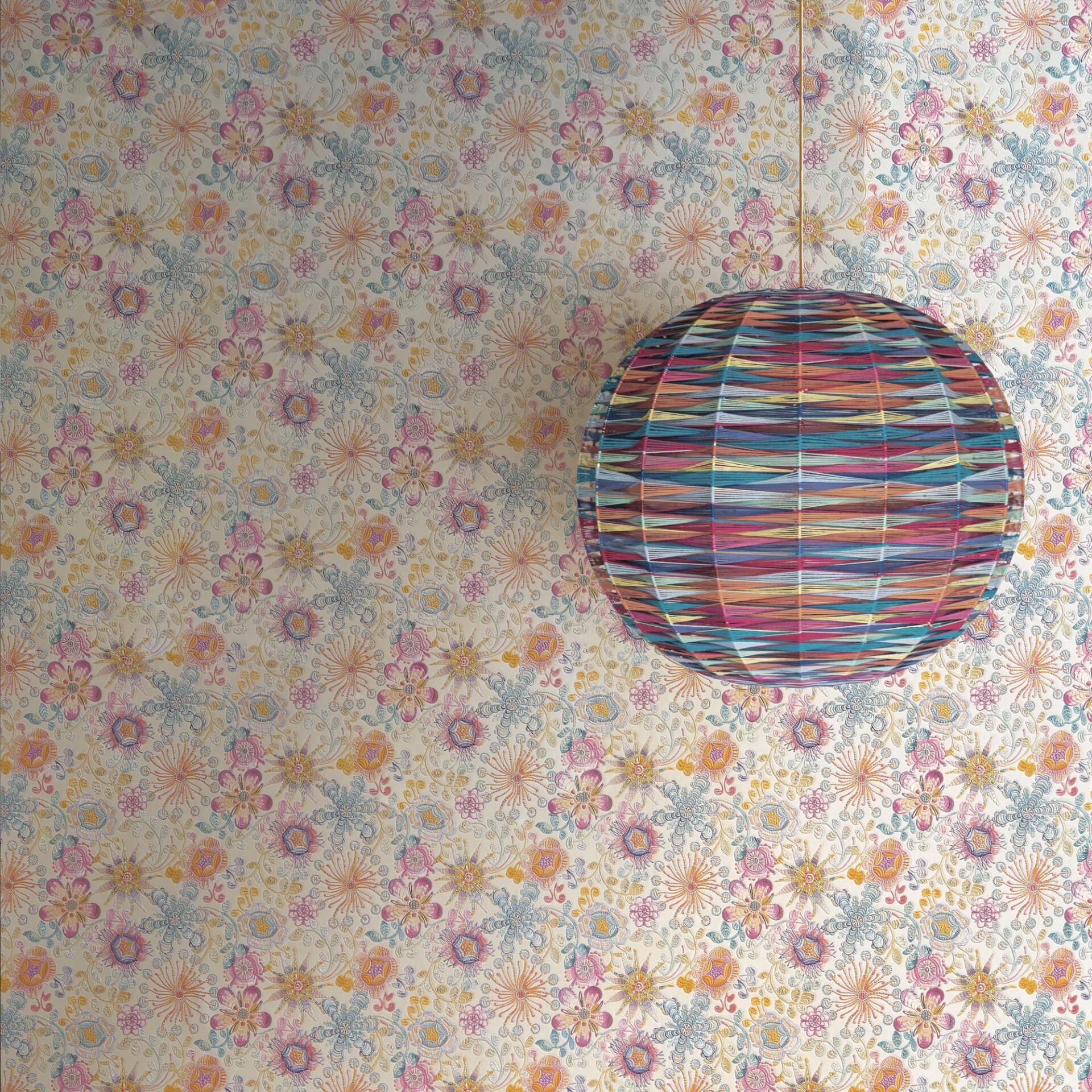 A colorful, striped spherical lampshade hanging against a wall covered in intricate floral wallpaper with muted pink, blue, and orange patterns.