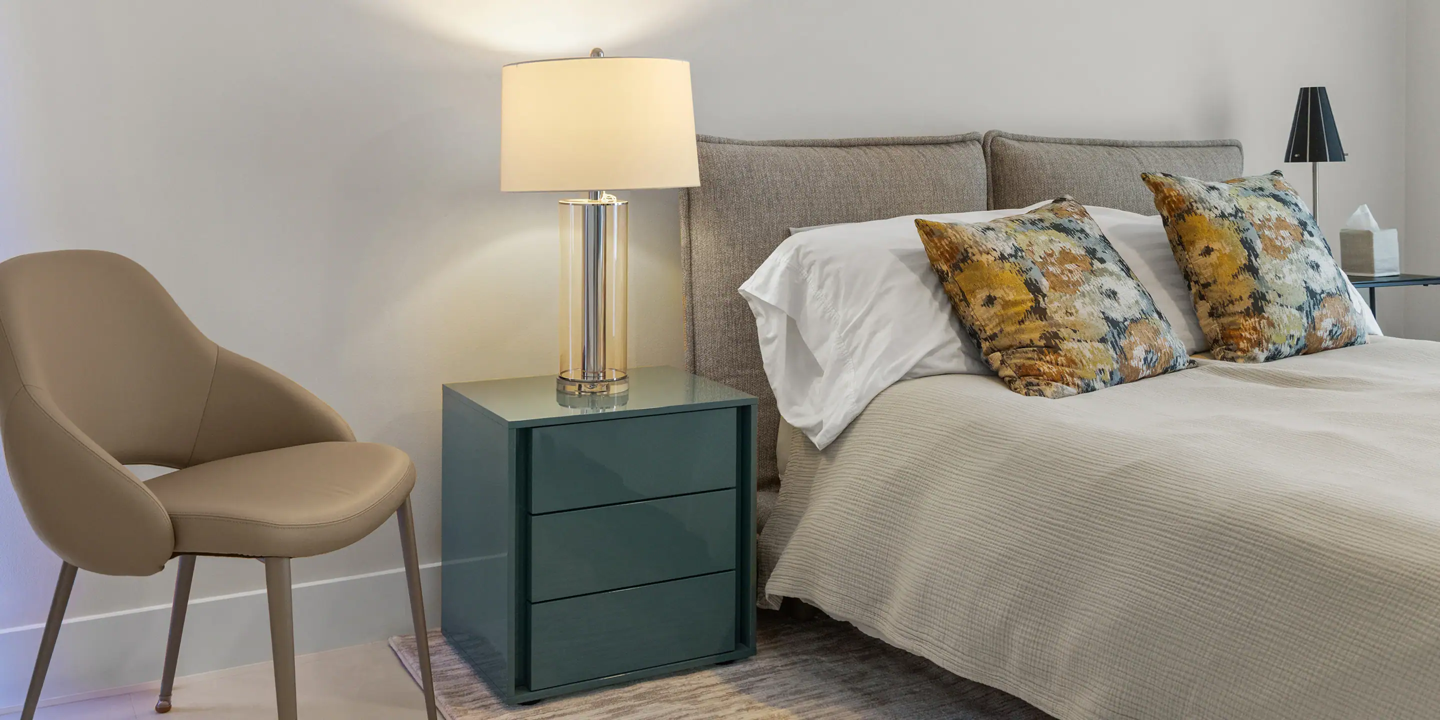 Cozy bedroom featuring a beige armchair, modern nightstand, and decorative pillows for comfort and s.