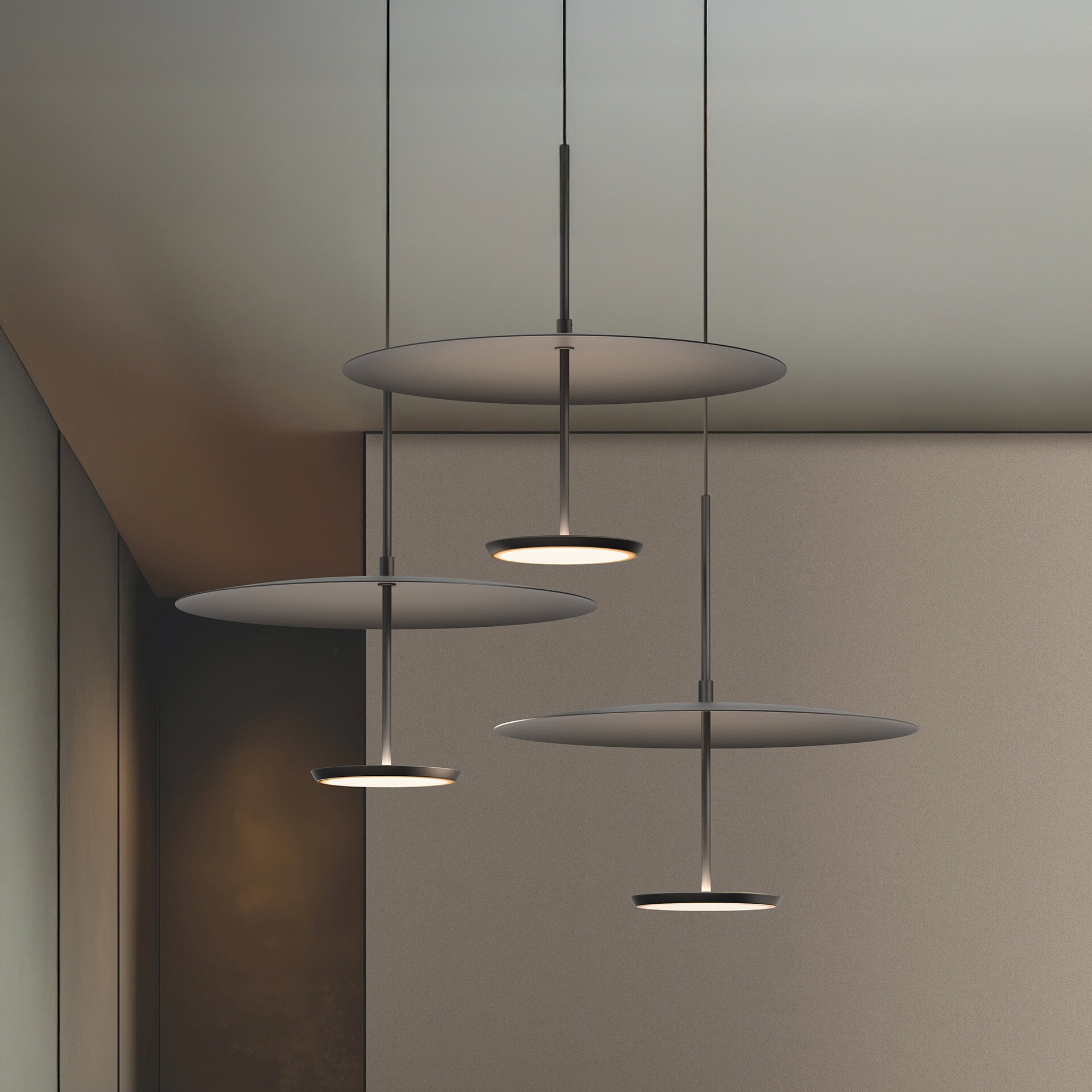 Four modern dark gray disc-shaped pendant lights with glowing circular centers hang at varying heights in a minimalist room with textured beige and brown walls.