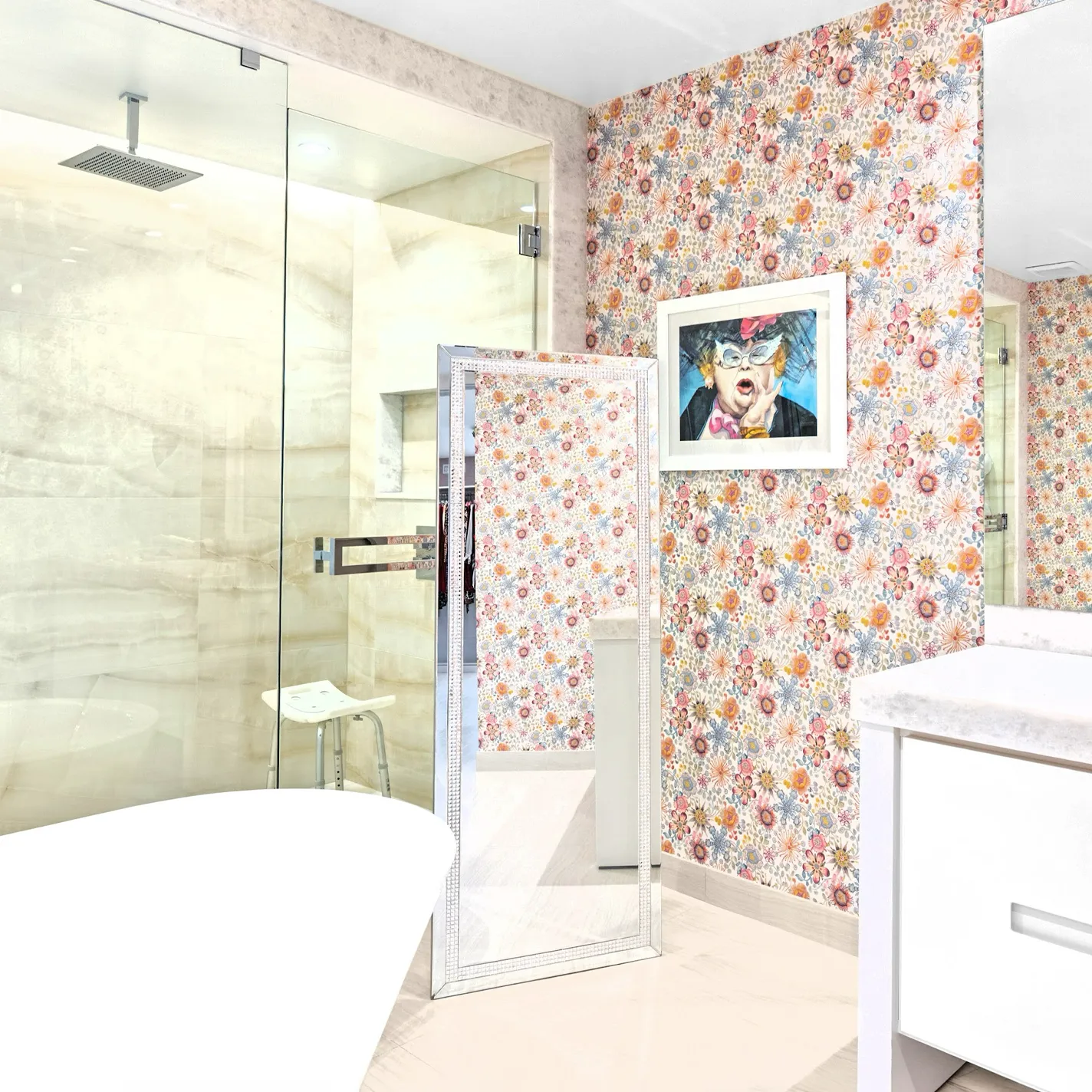 A modern bathroom with floral wallpaper, a glass shower, a white freestanding tub, a full-length mirror, and a framed artwork of a person with exaggerated features.