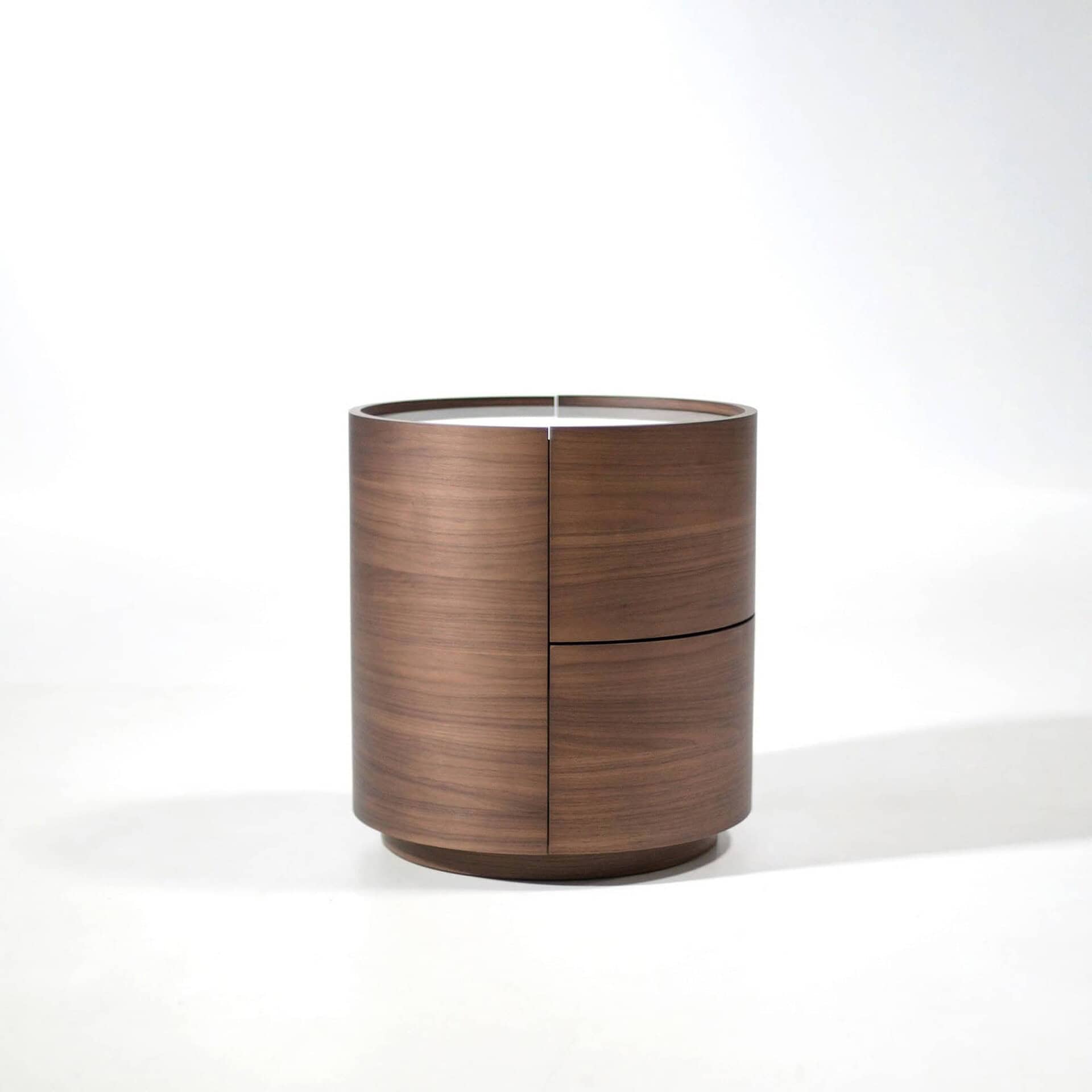 A cylindrical dark brown wood nightstand with a light top inset and subtle drawer lines, against a white background.