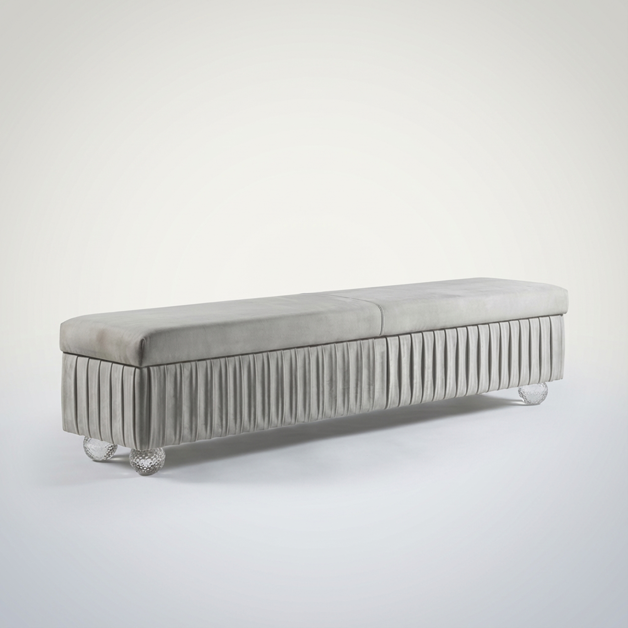 A long, light grey velvet bench with a pleated skirt design and clear, textured spherical legs, set against a plain light background.