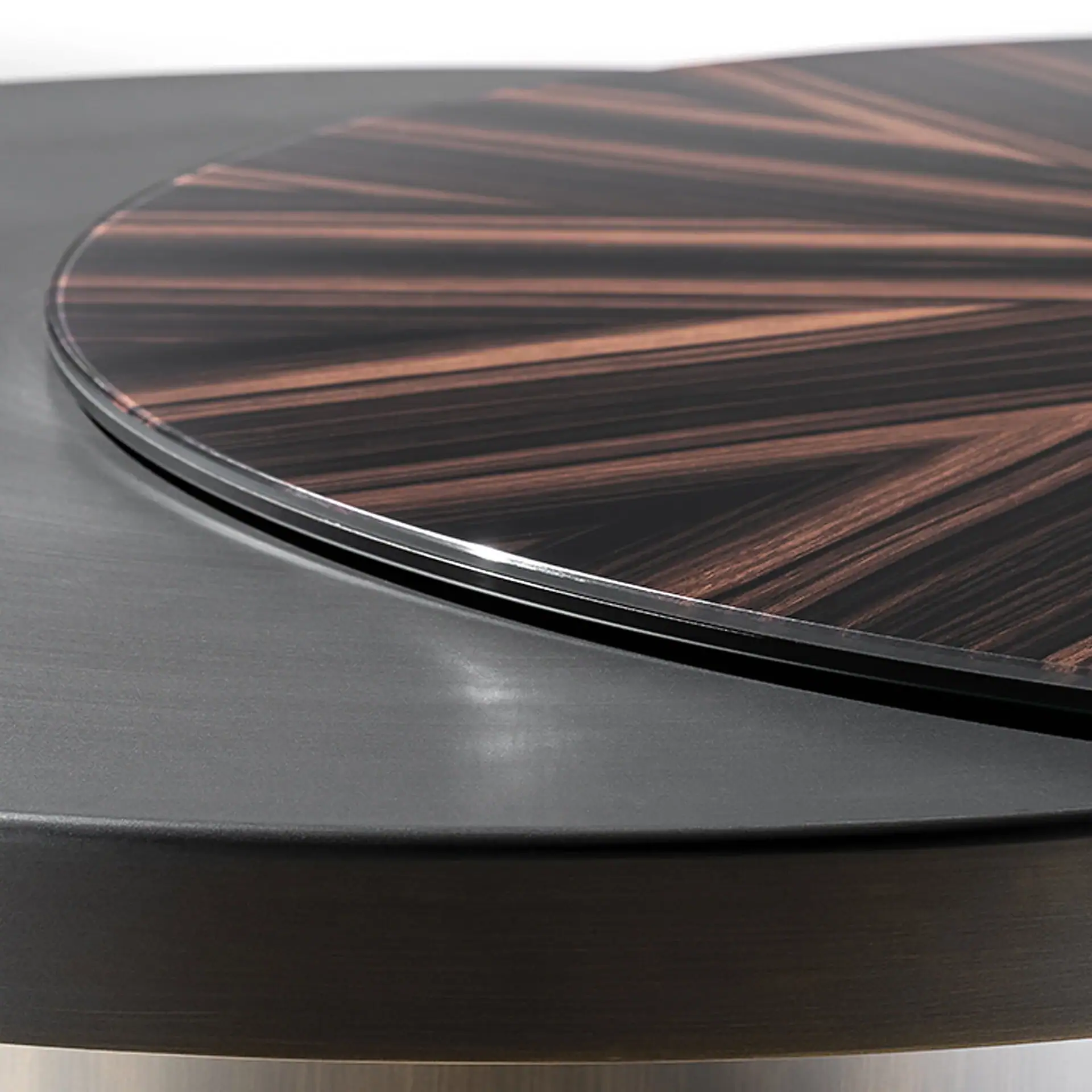 Close-up of a circular table with a dark, glossy, wood grain rotating top on a matte dark gray base.