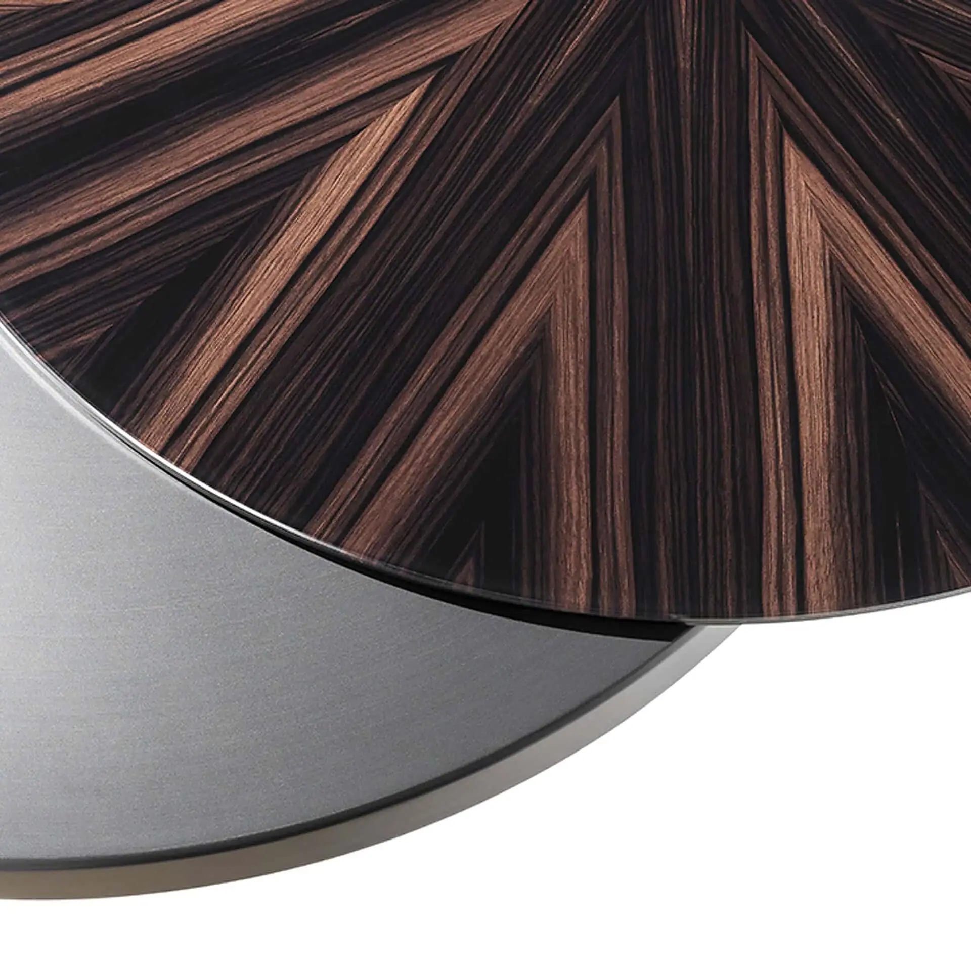Close-up of a circular surface with a dark brown chevron wood grain pattern and a brushed silver-gray metallic edge.