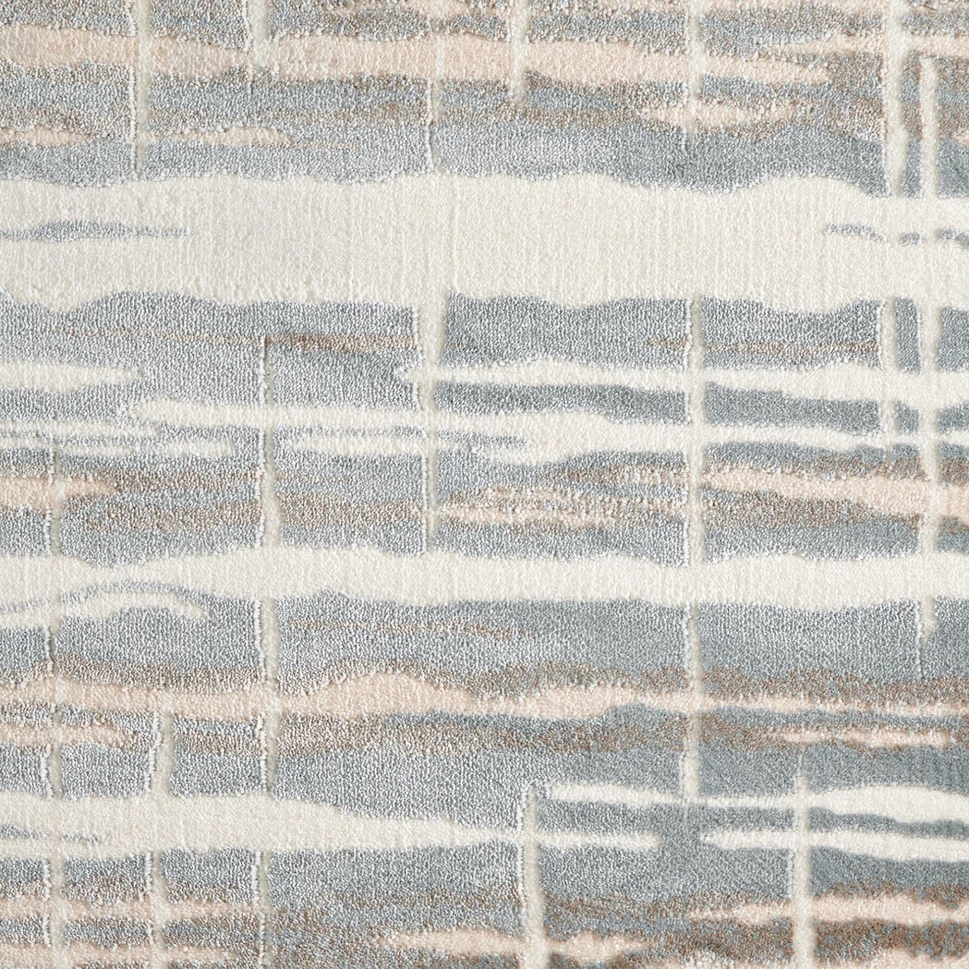 Close-up of a textured rug with an abstract, grid-like pattern in off-white, light blue-grey, and warm beige.