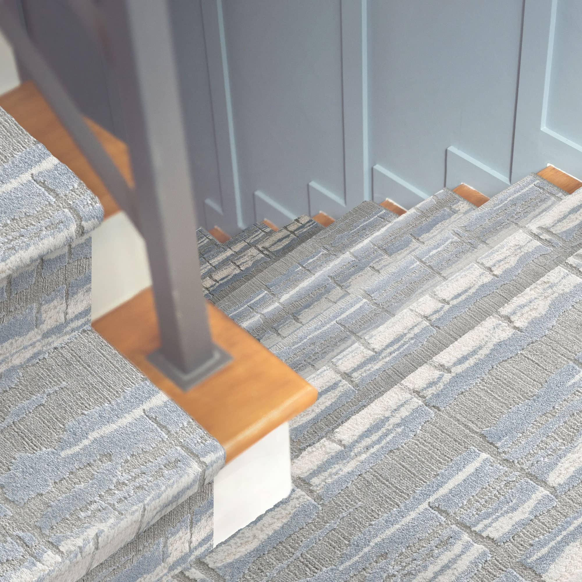A carpeted staircase with a modern abstract runner in blue, gray, and white, alongside a paneled blue-gray wall and a dark metal railing.
