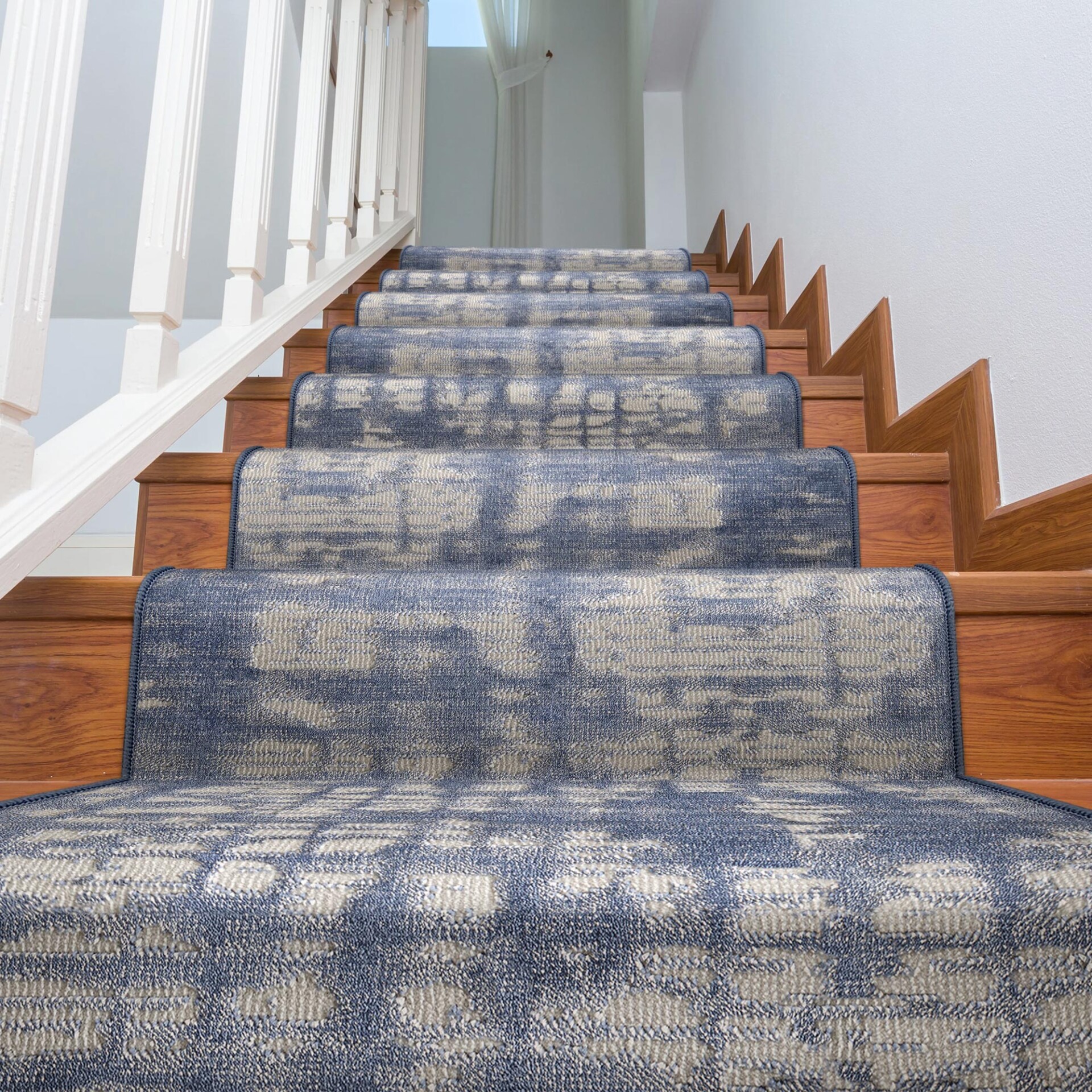 A wooden staircase with a blue and beige abstract patterned stair runner, white balusters, and white walls, viewed from a low angle looking up.