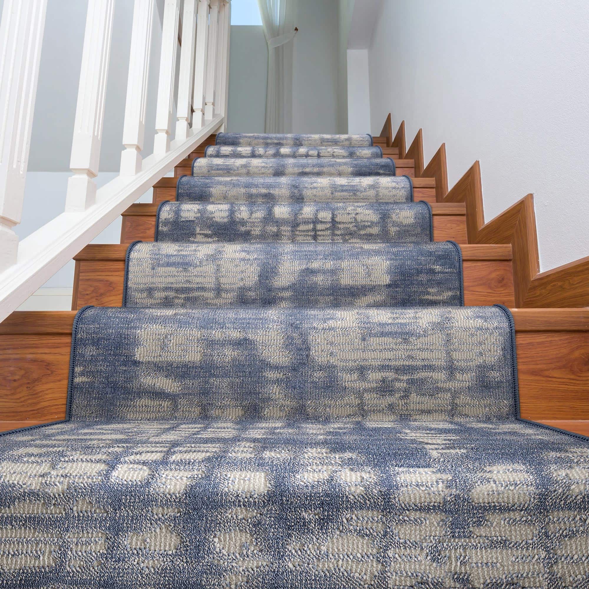 A wooden staircase with a blue and beige abstract patterned stair runner, white balusters, and white walls, viewed from a low angle looking up.