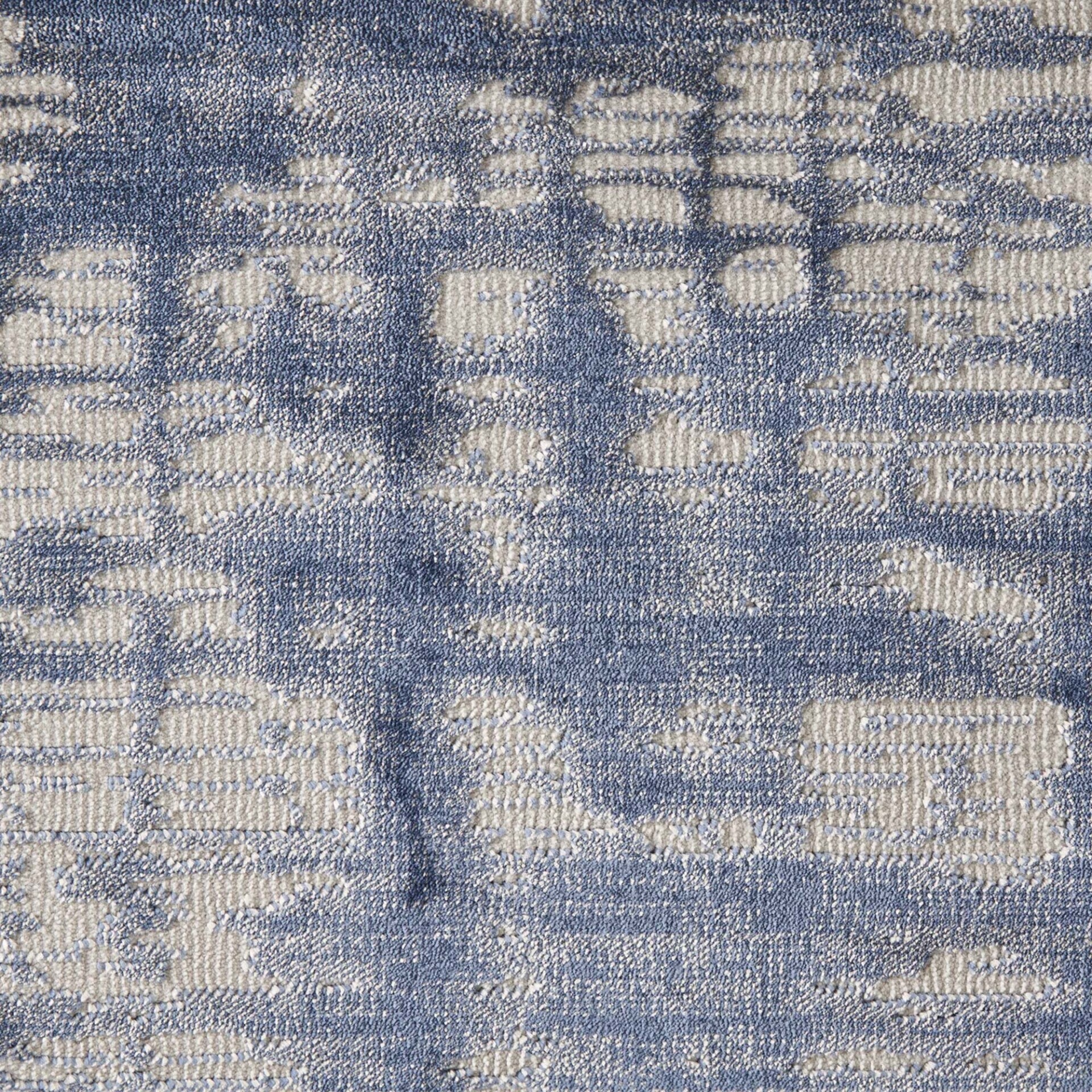 Close-up of a blue and off-white textured fabric or carpet with an abstract, blocky pattern and visible fiber texture.