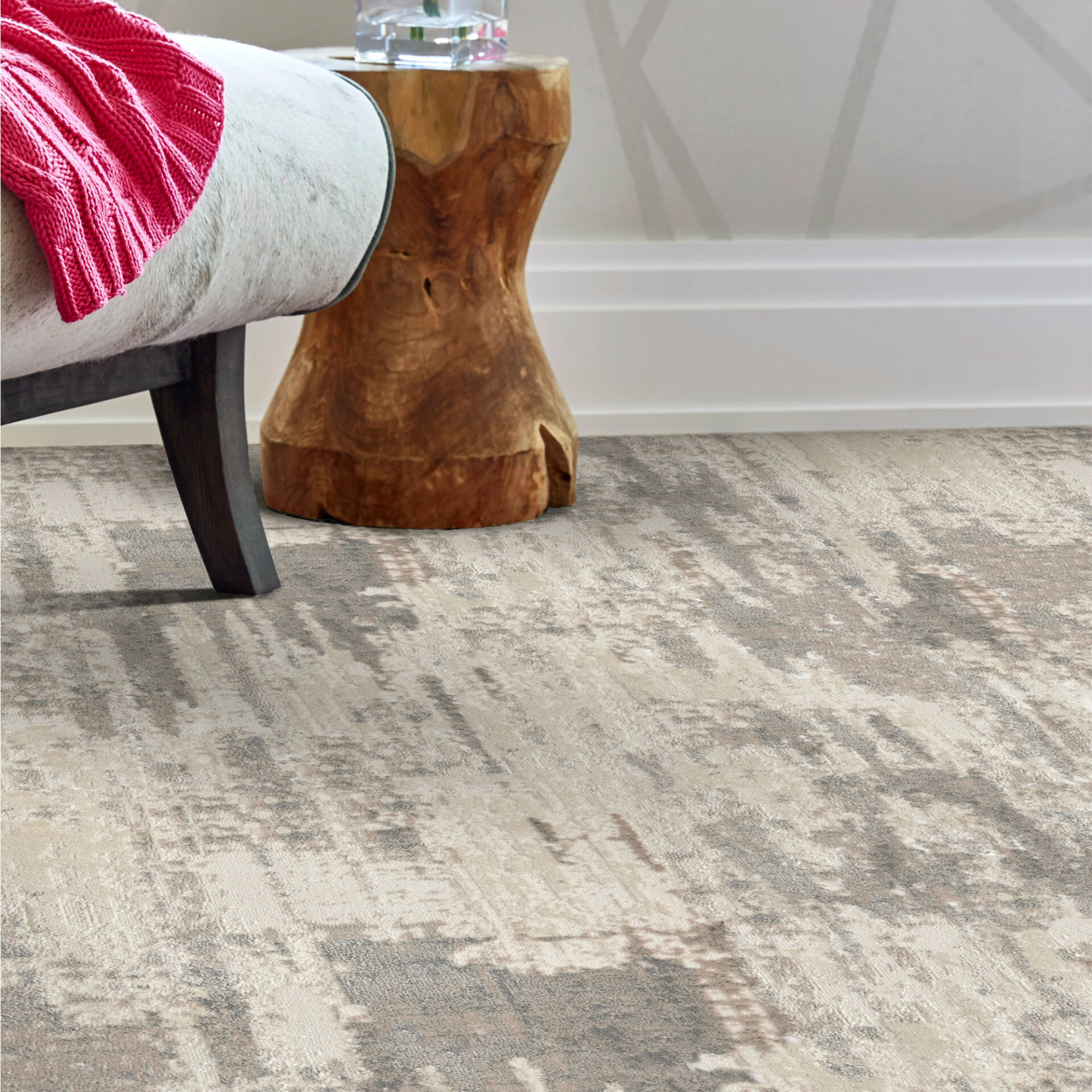 A room featuring a light-colored abstract patterned carpet. A white upholstered bench with a pink throw and a natural wood side table are partially visible.