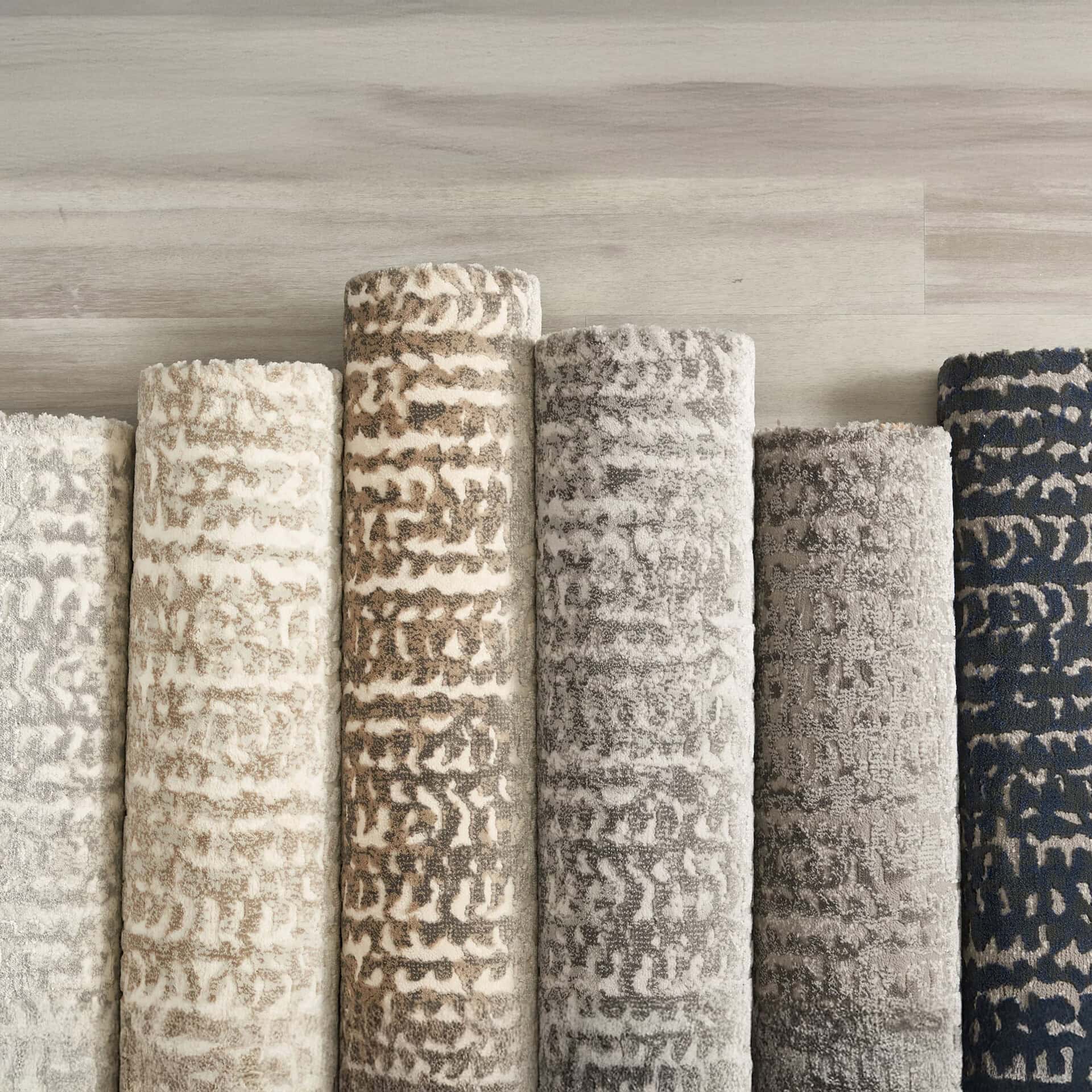 Luxurious carpet rolls with intricate designs in neutral and navy hues, perfect for elegant home decor.
