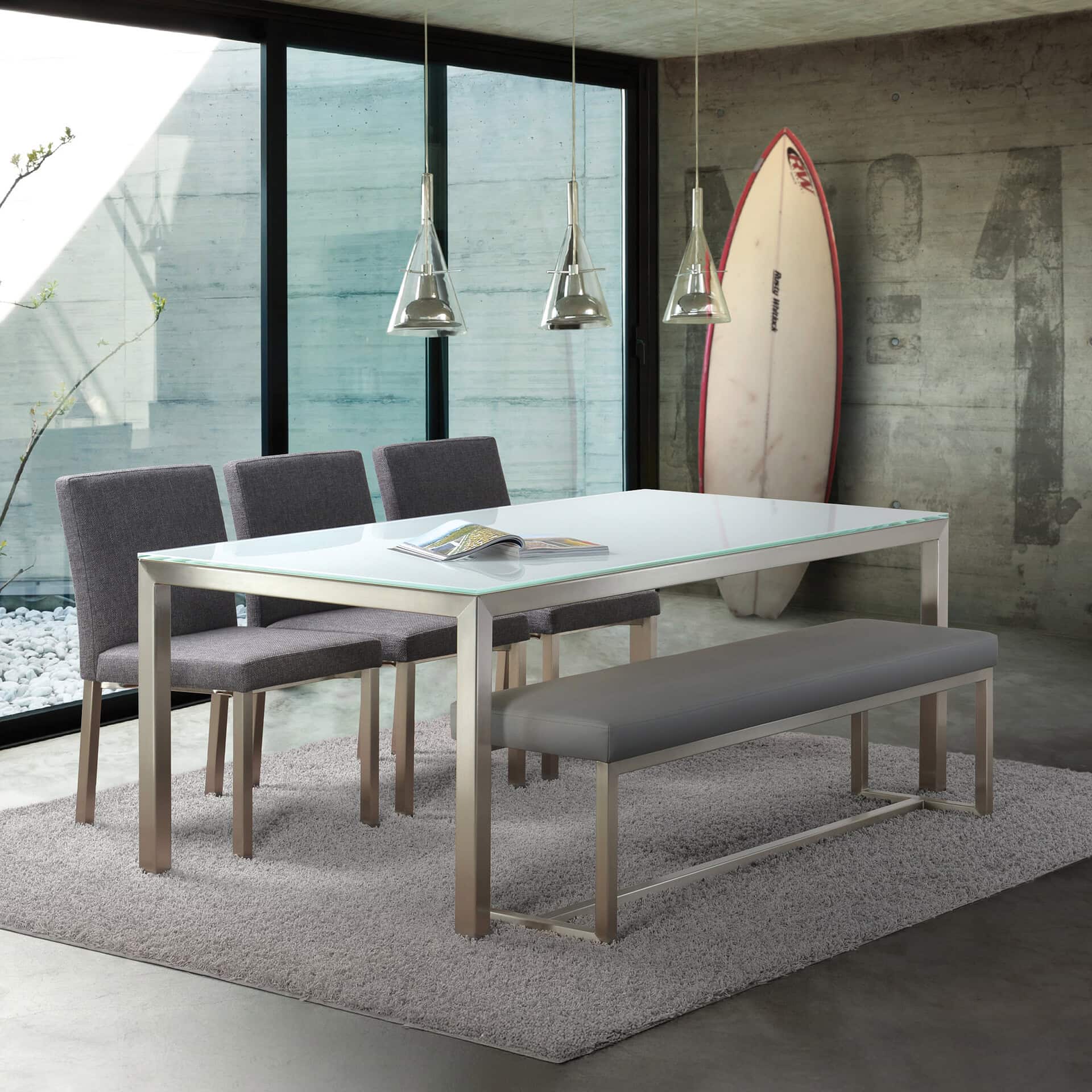 Spacious dining room with contemporary table, upholstered gray seating, and surfboard decor, featuring large windows for natural light.