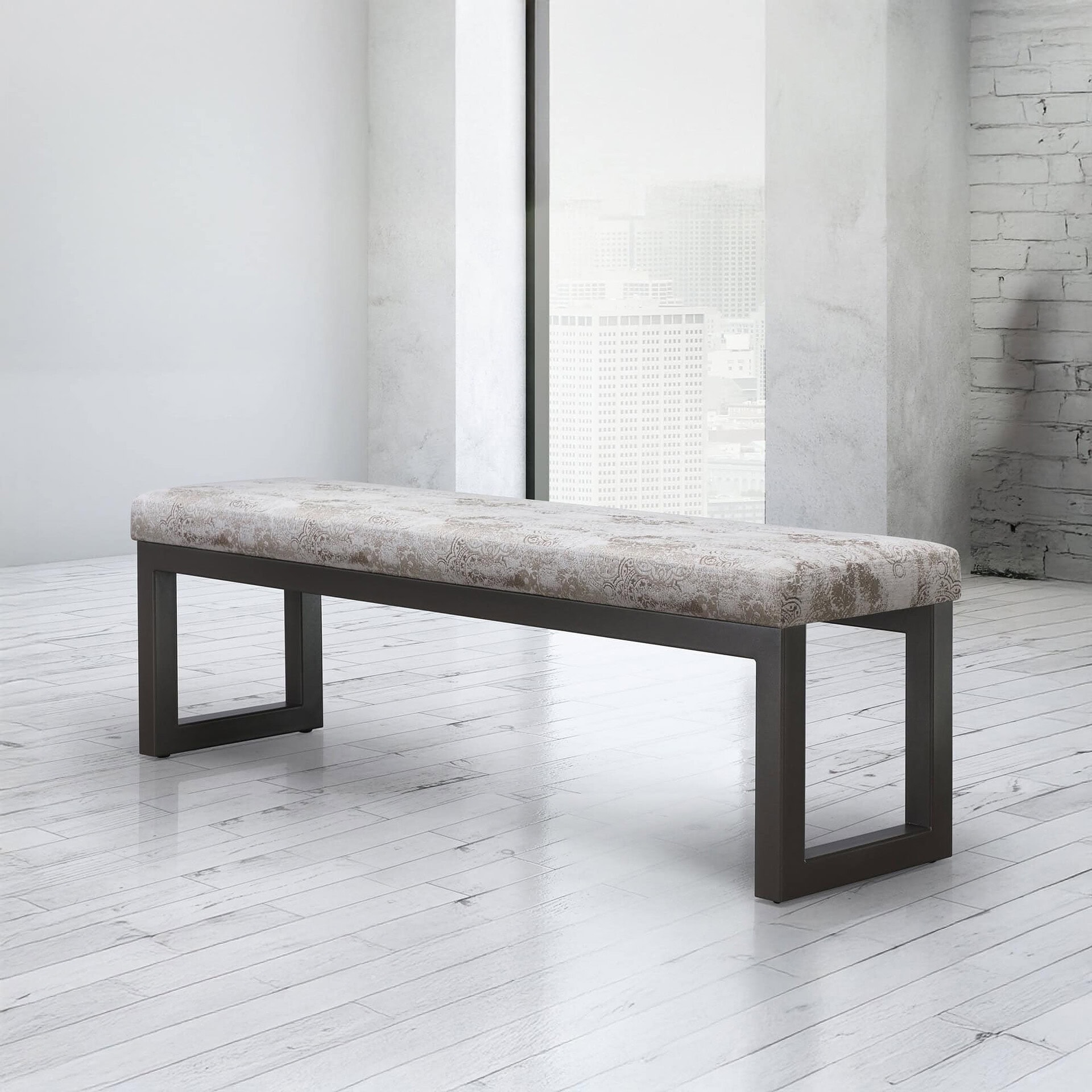 A modern upholstered bench with a patterned beige cushion and dark metal legs in a bright, minimalist room with a city view from a large window.