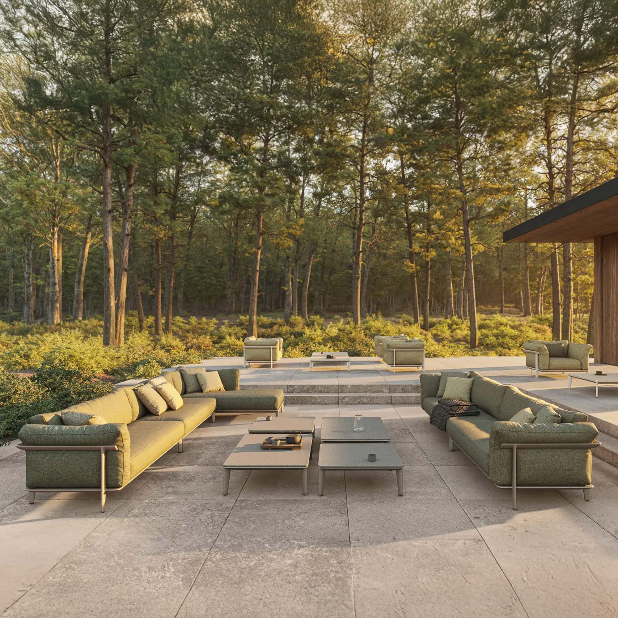 Modern outdoor sectional sofas in a natural setting with lush trees and contemporary coffee tables.