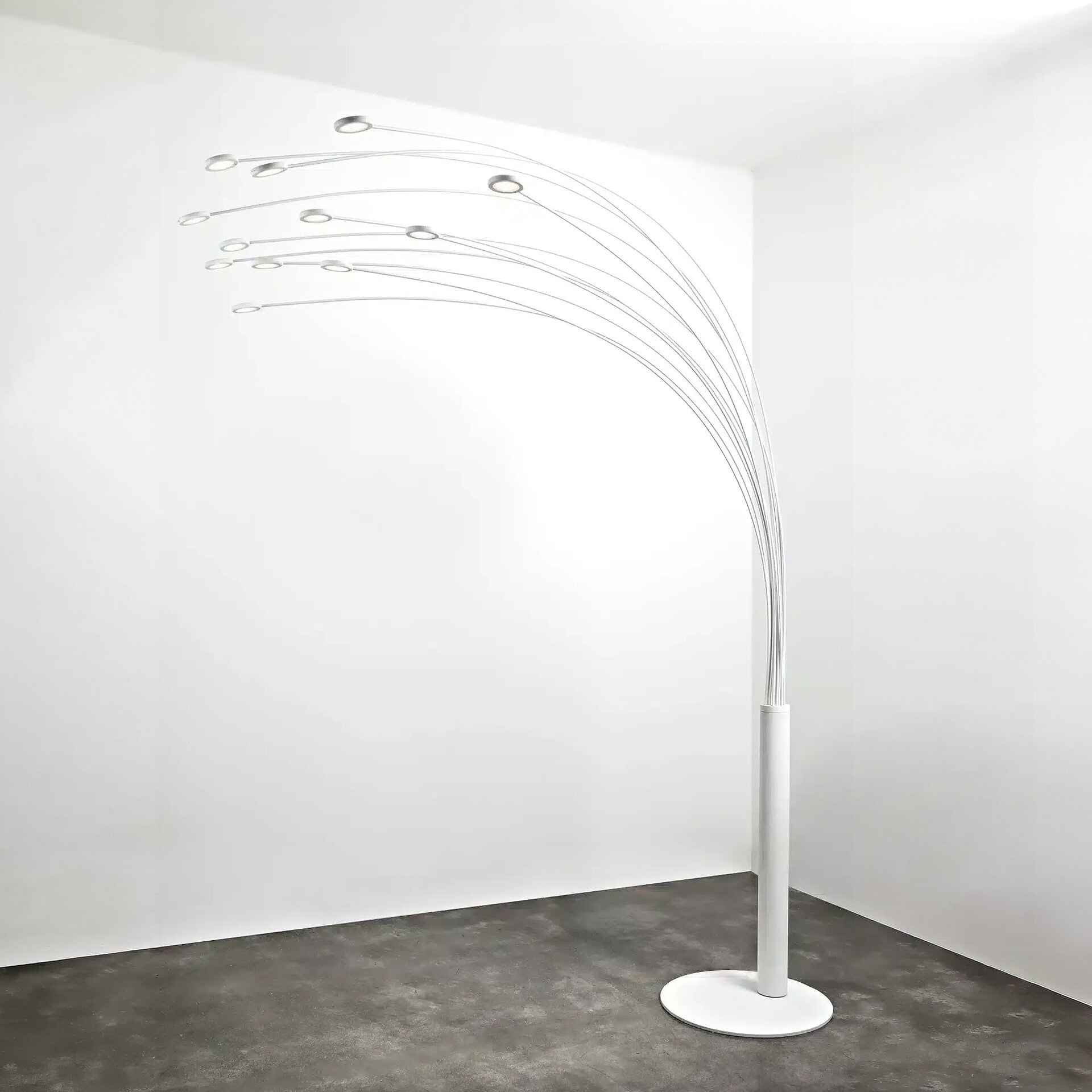 A modern white floor lamp with multiple thin, arching silver arms, each ending in a circular light, standing in a minimalist white room with a dark floor.