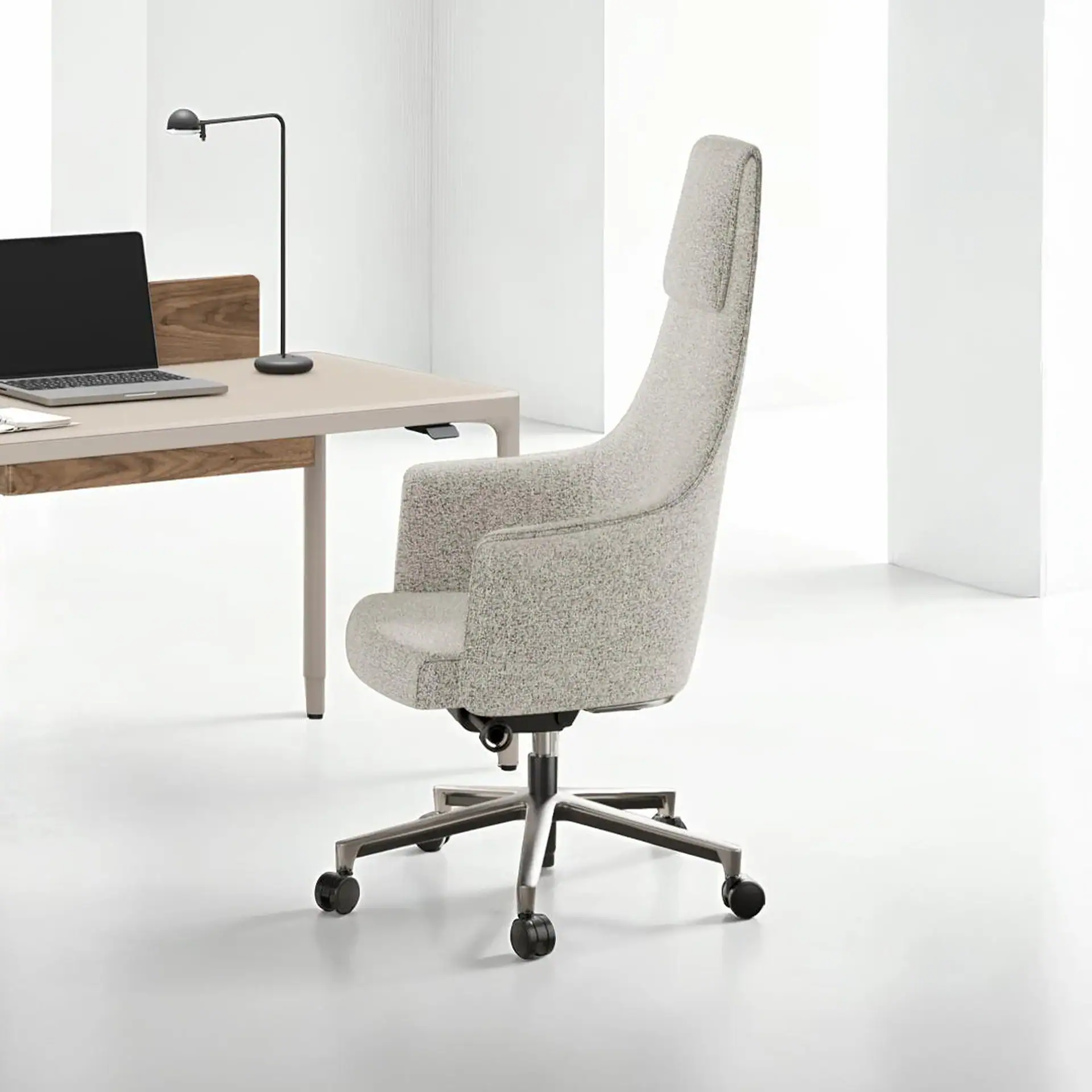A modern office scene with a light gray ergonomic office chair, a minimalist desk with a laptop, and a black desk lamp against a white background.