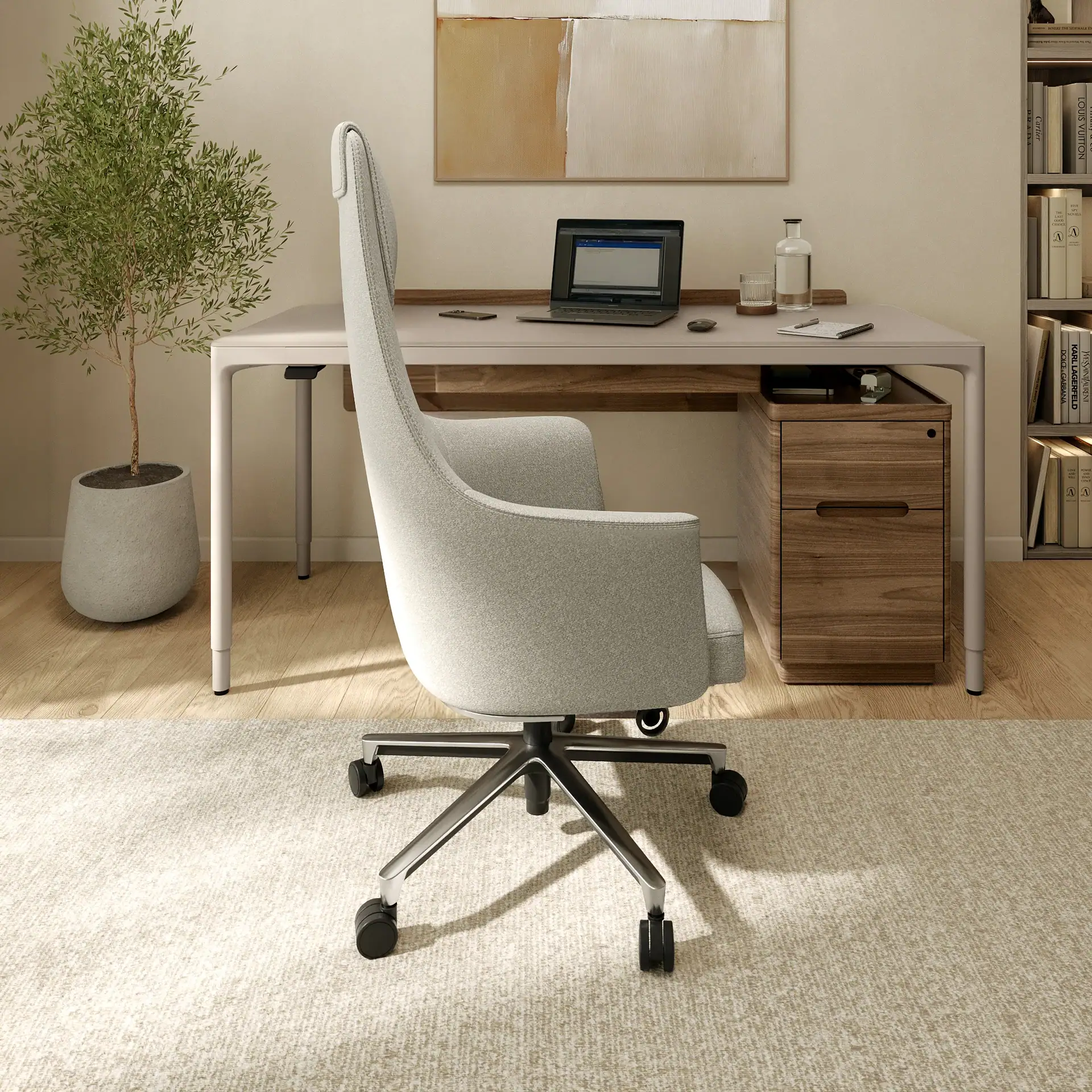 A modern home office featuring a light gray ergonomic chair, a minimalist desk with a laptop and water, a potted plant, and a bookshelf with designer books.
