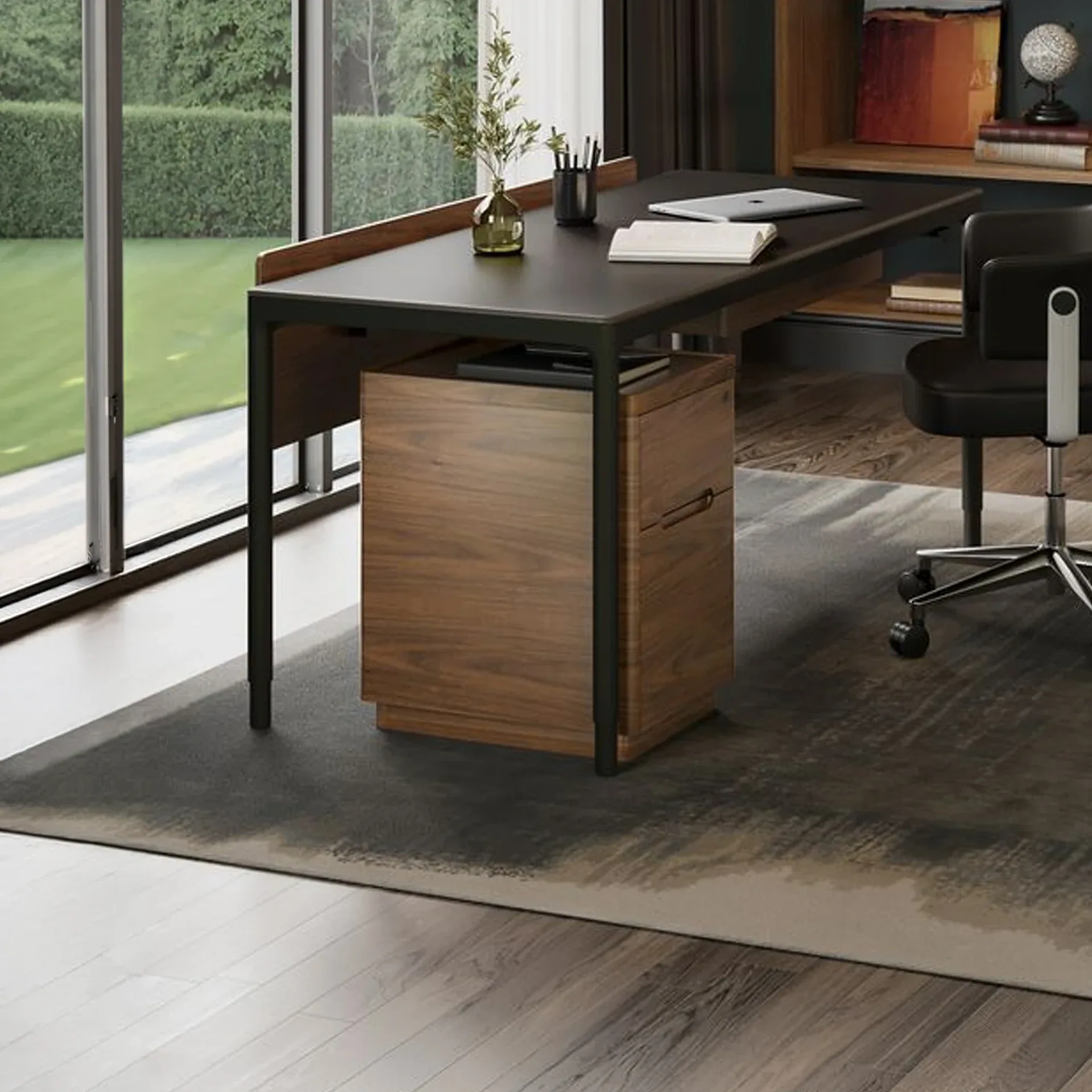 A modern home office with a dark desk, black office chair, wooden filing cabinet, and a large window overlooking a green lawn.