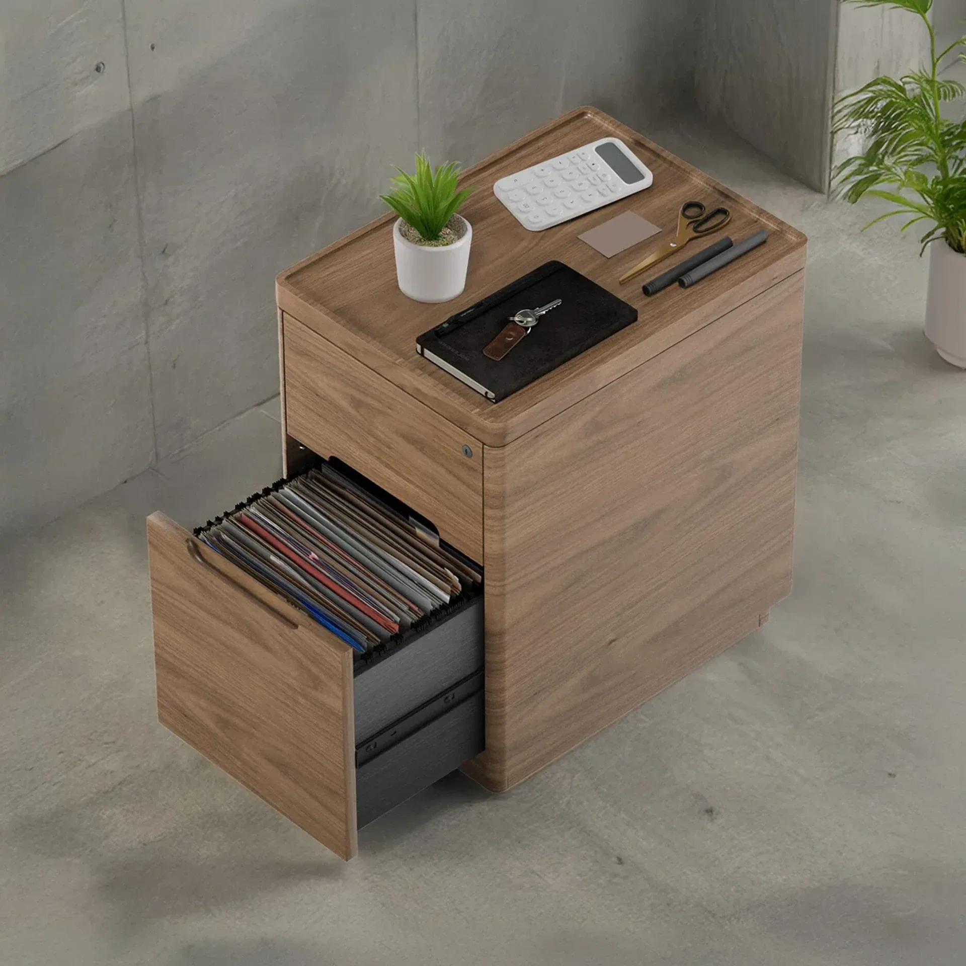 A wooden filing cabinet with rounded corners, one drawer open showing files, and a calculator, plant, and keys on top.