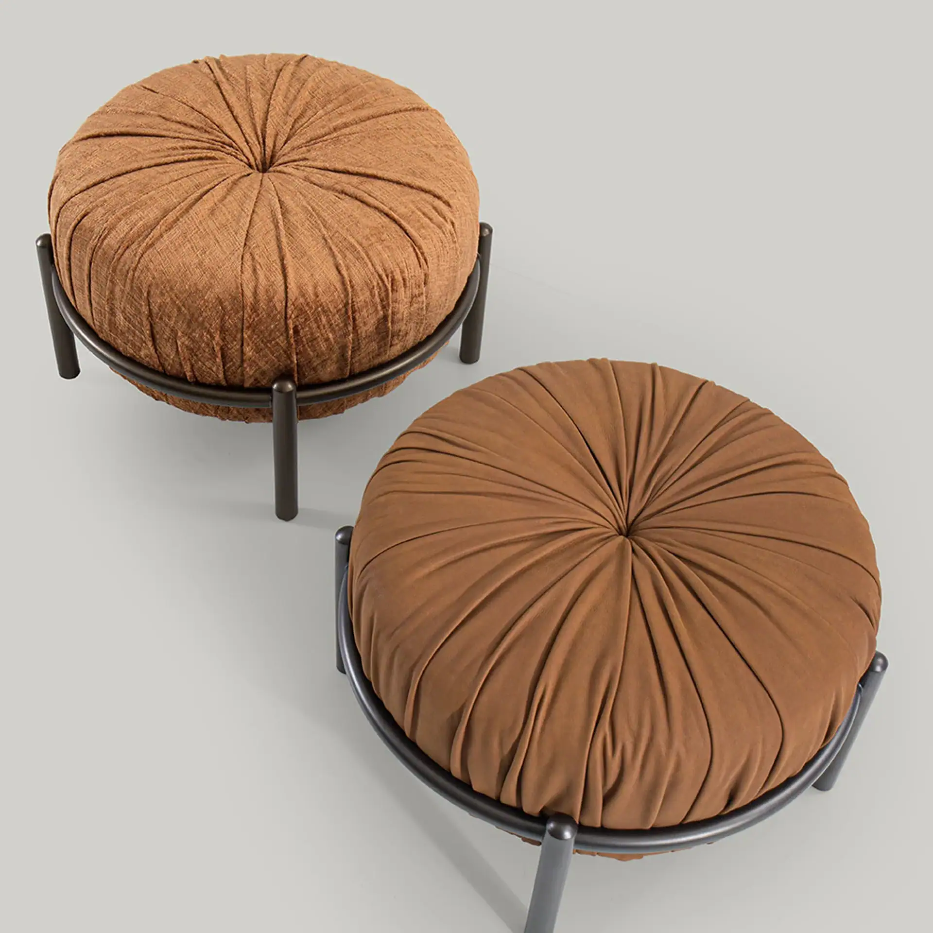 Two round brown pleated ottomans with dark grey metal frames on a light grey background.