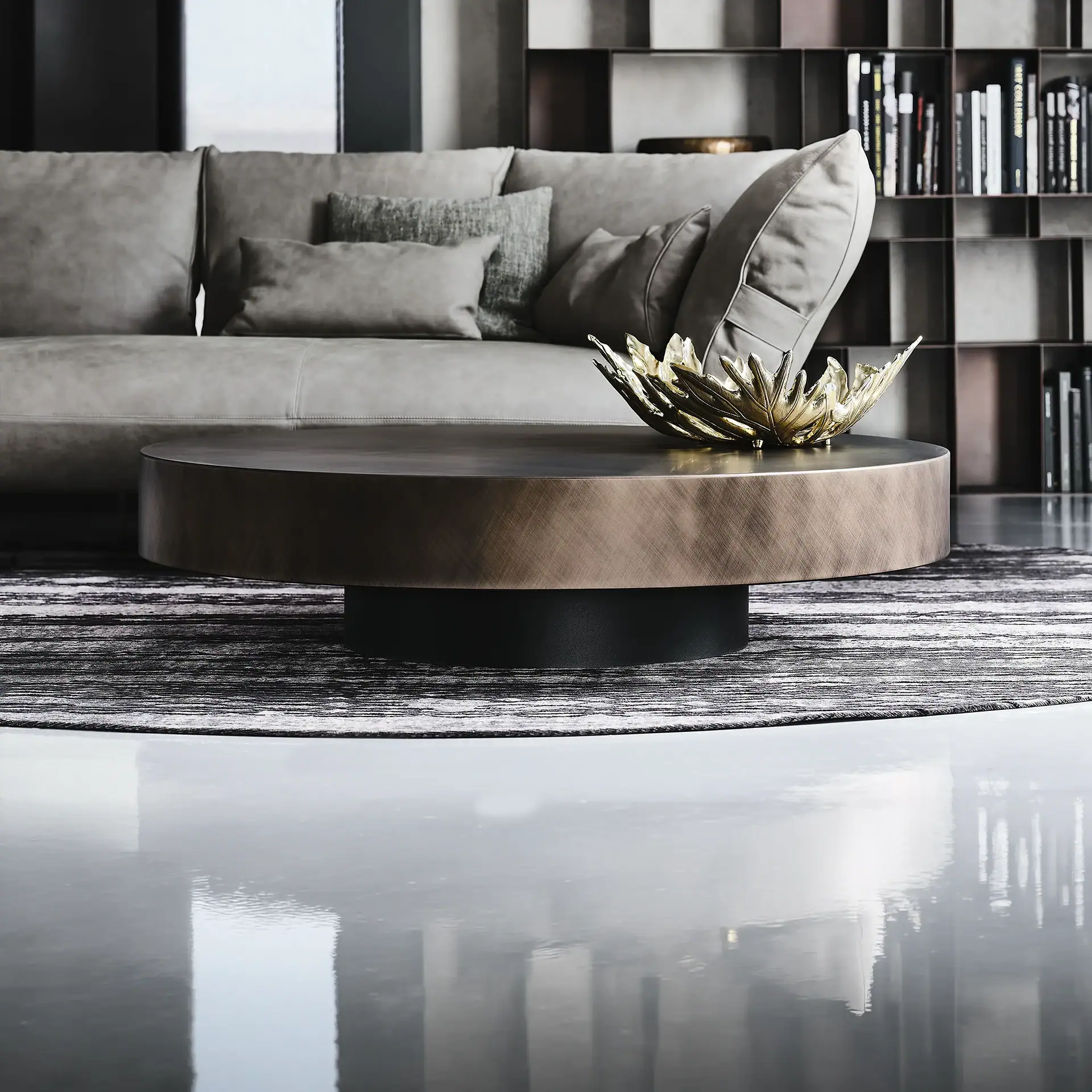 A modern living room with a gray sofa, a round bronze coffee table with a gold leaf sculpture, and a striped rug on a reflective floor.