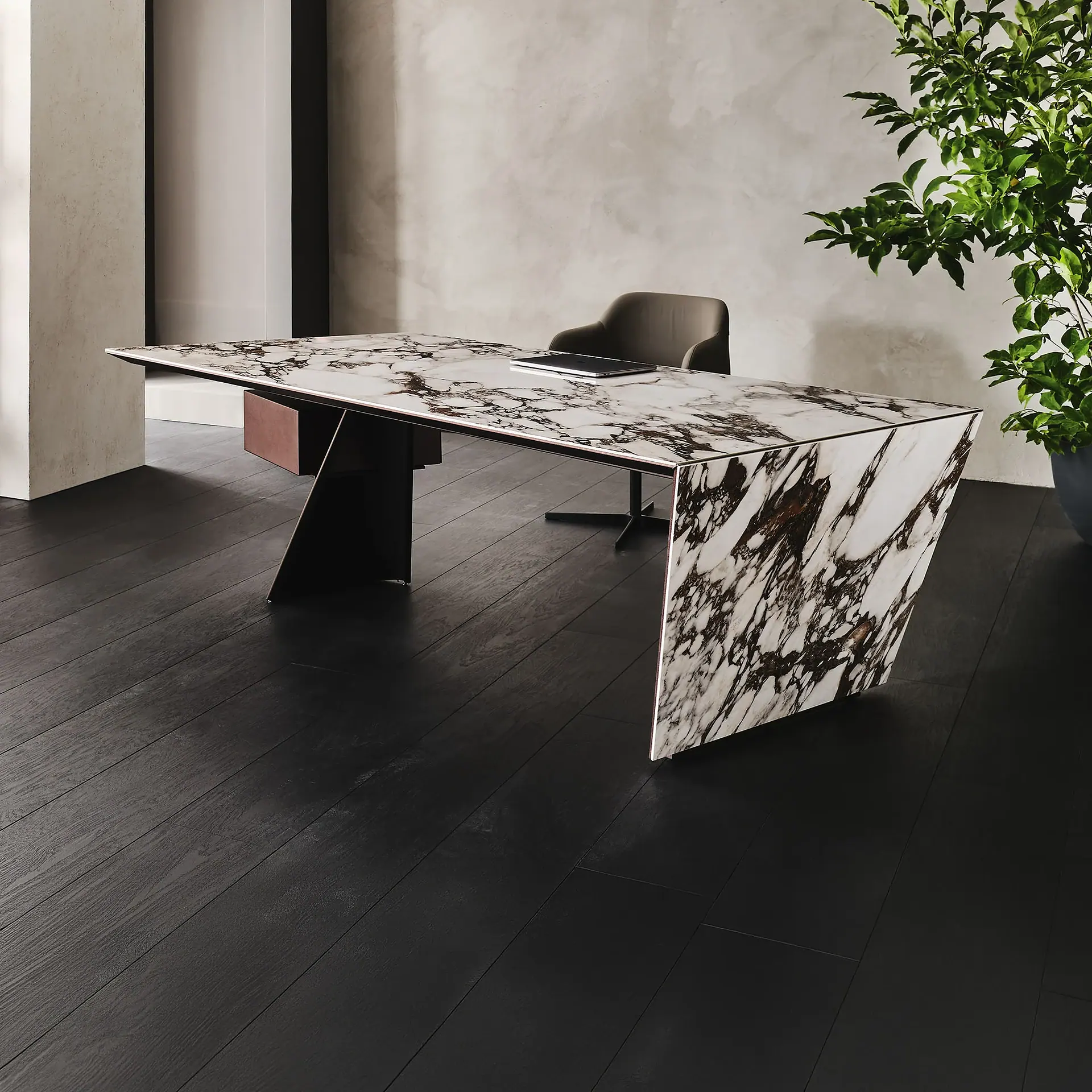 A modern office with a white and dark veined marble desk, a dark upholstered chair, dark wood floors, and a green potted plant.