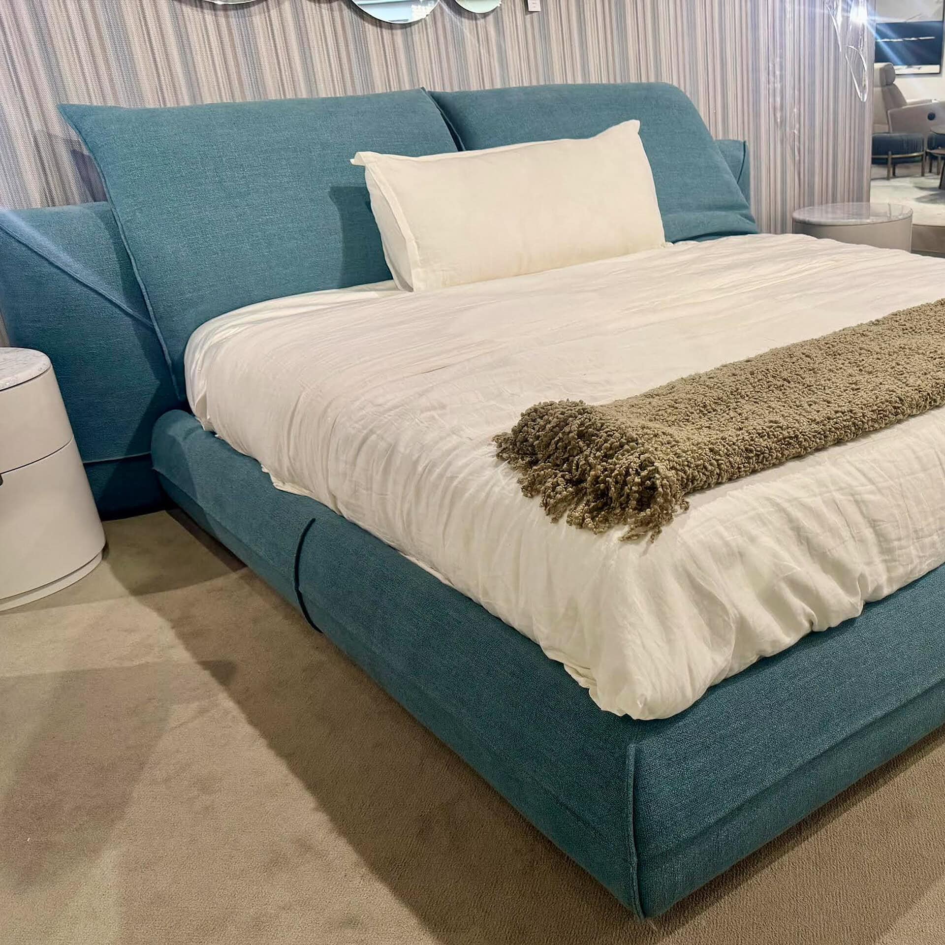 Modern blue upholstered bed with white bedding and plush throw.
