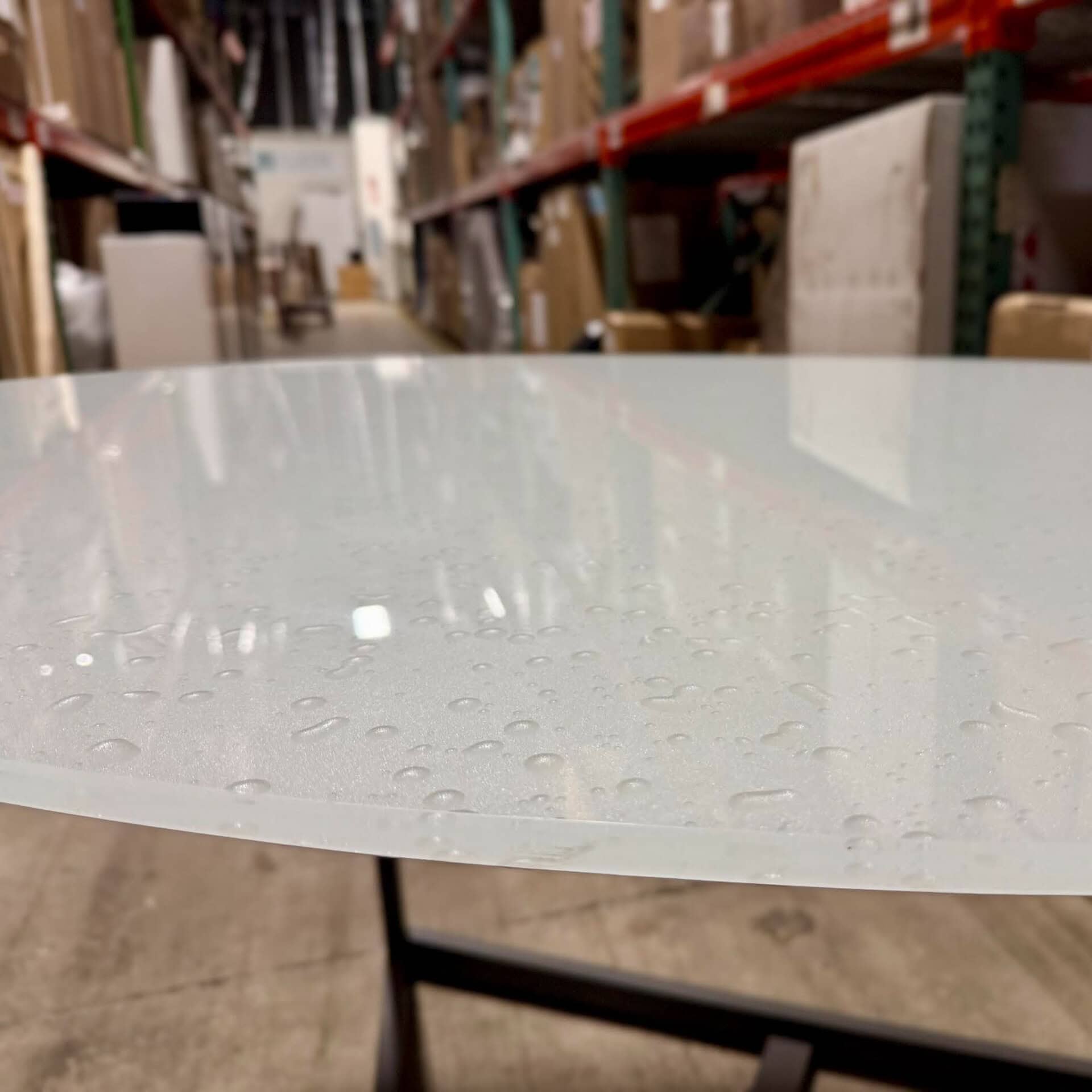 Sleek glass table with water droplets, showcased in a warehouse environment for modern furniture dis.