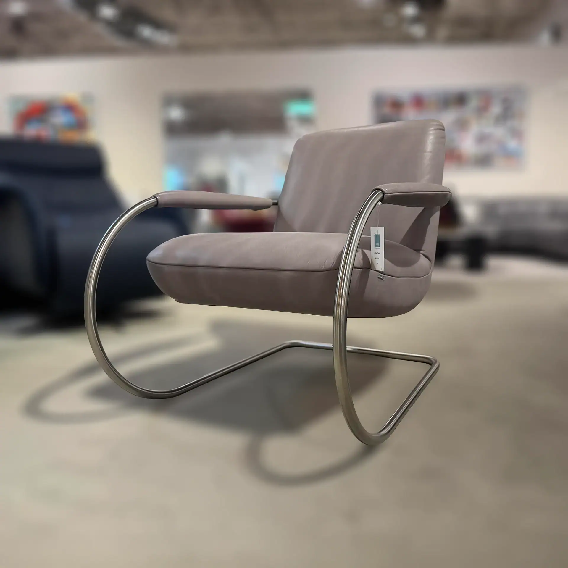 A light taupe leather armchair with a polished chrome cantilever frame in a showroom.