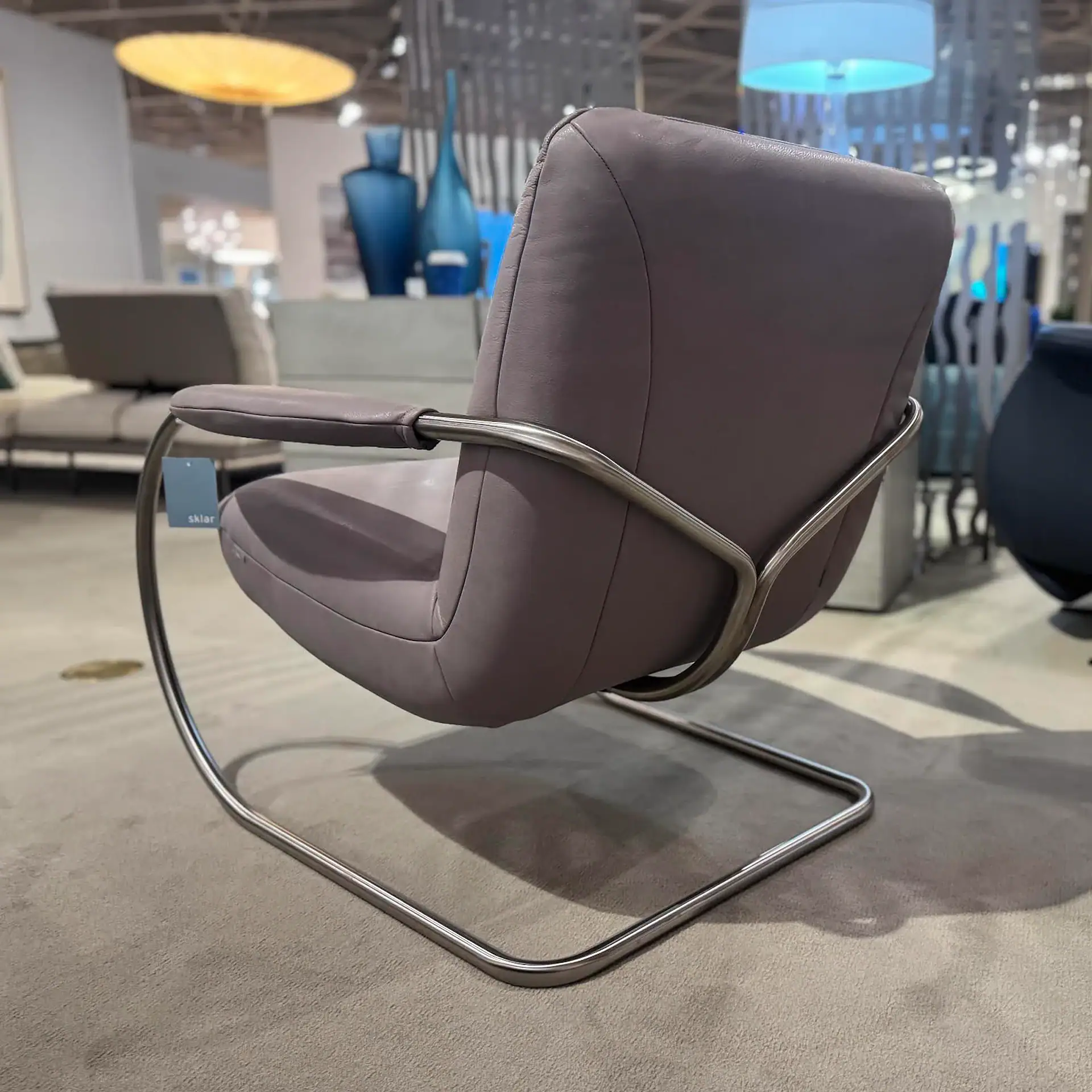 A modern cantilever armchair with purple-grey upholstery and a silver metal frame, in a showroom setting.