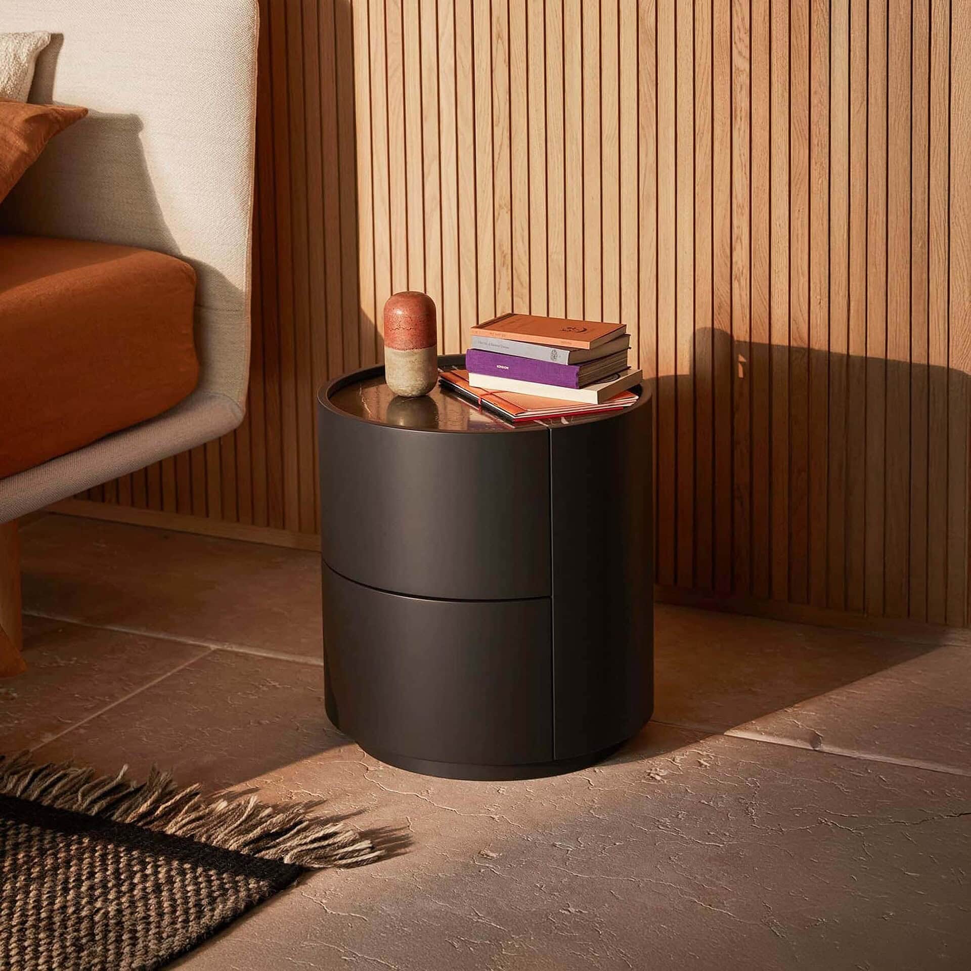 Black round side table with decorative vase and stacked books in a contemporary living room.