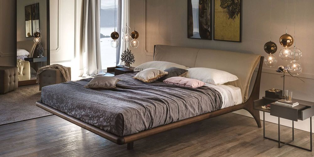 A luxurious modern bedroom with a low-profile bed, upholstered headboard, and pendant lights. A large window overlooks a lake and mountains. The Nelson Upholstered Bed