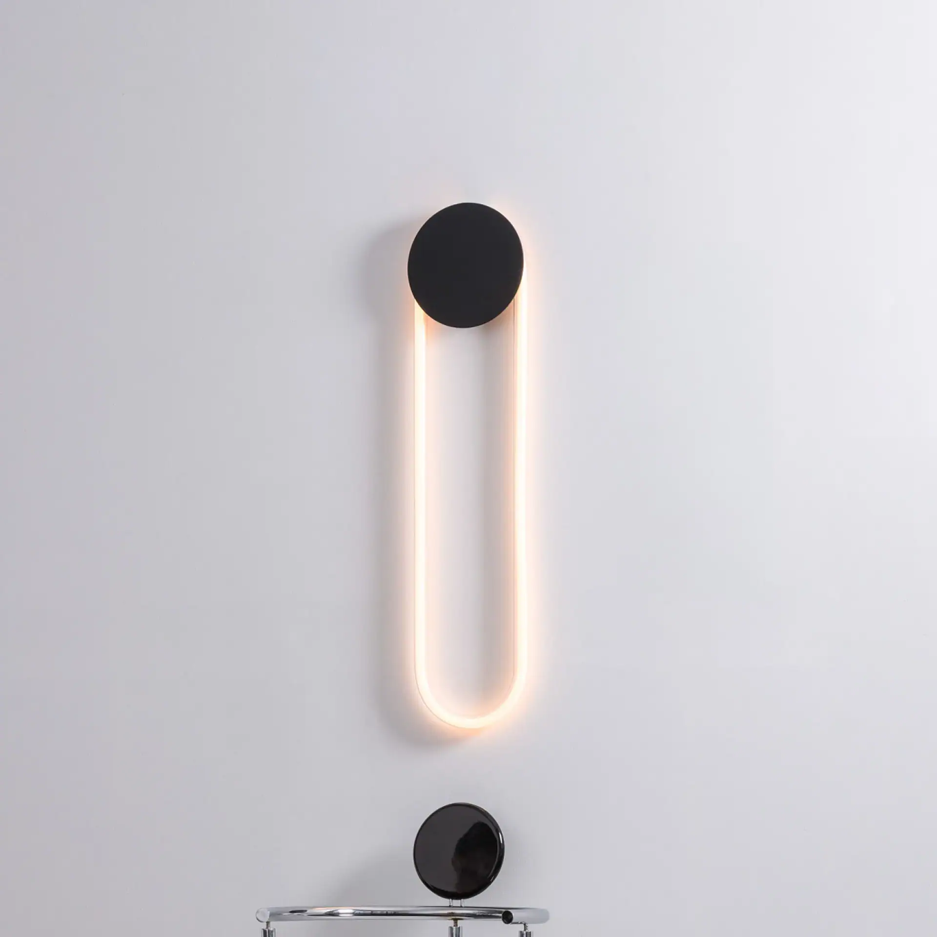 RA Sculptural Wall Sconce with illuminated loop and round base on wall.