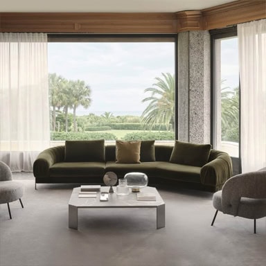 Elegant green sofa with beige pillows in a sunlit living room with large windows.