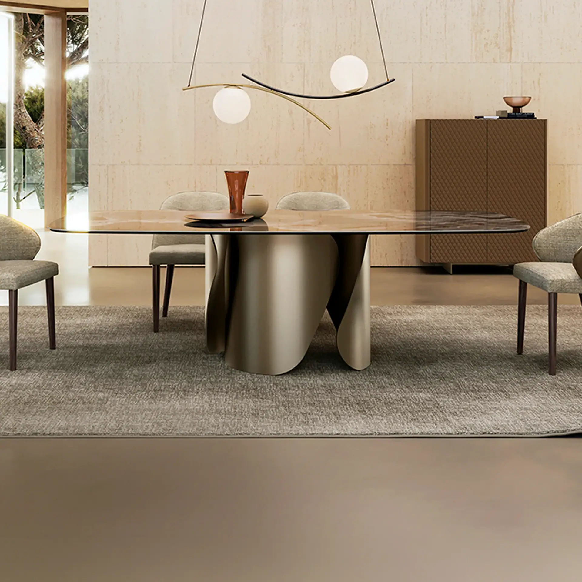 A modern dining room with a glass-top table, sculptural metallic base, four upholstered chairs, and a contemporary chandelier. A textured cabinet and travertine wall are in the background.