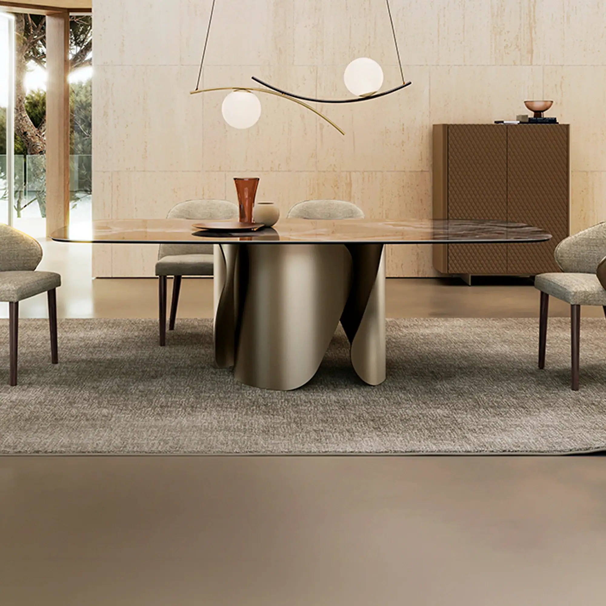A modern dining room with a glass-top table, sculptural metallic base, four upholstered chairs, and a contemporary chandelier. A textured cabinet and travertine wall are in the background.