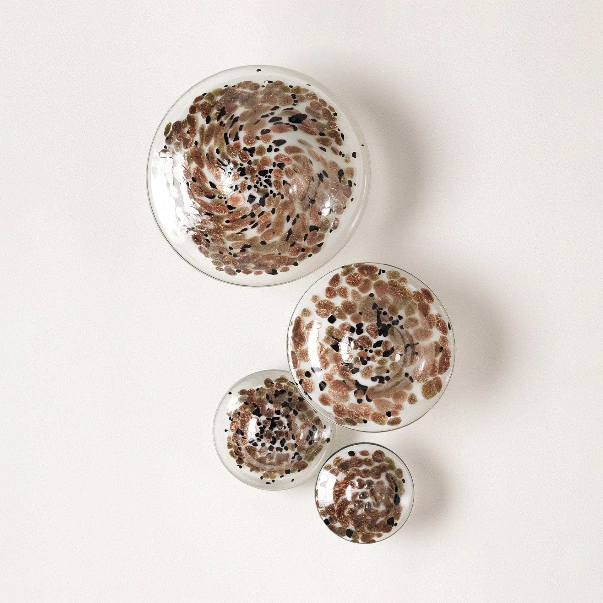 Four circular glass wall art pieces with shimmering bronze and black speckled patterns, arranged diagonally on a light-colored wall.