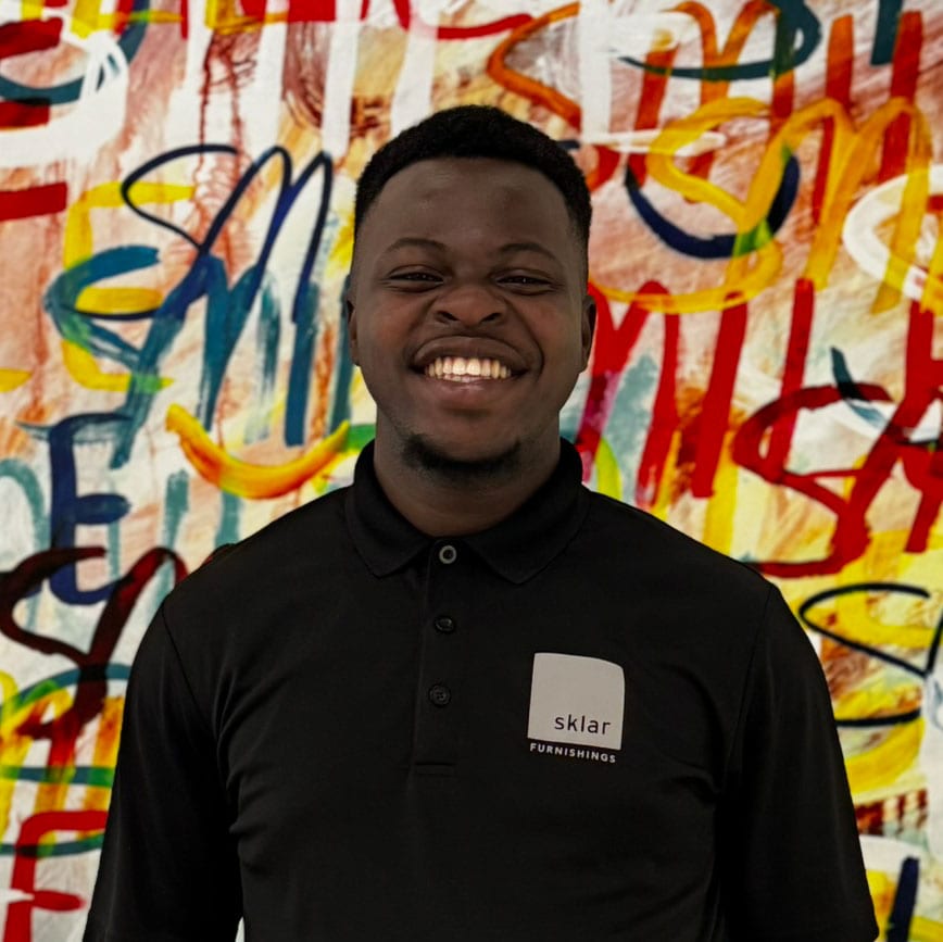 Employee wearing Sklar Furnishings branded polo shirt in front of colorful graffiti wall.
