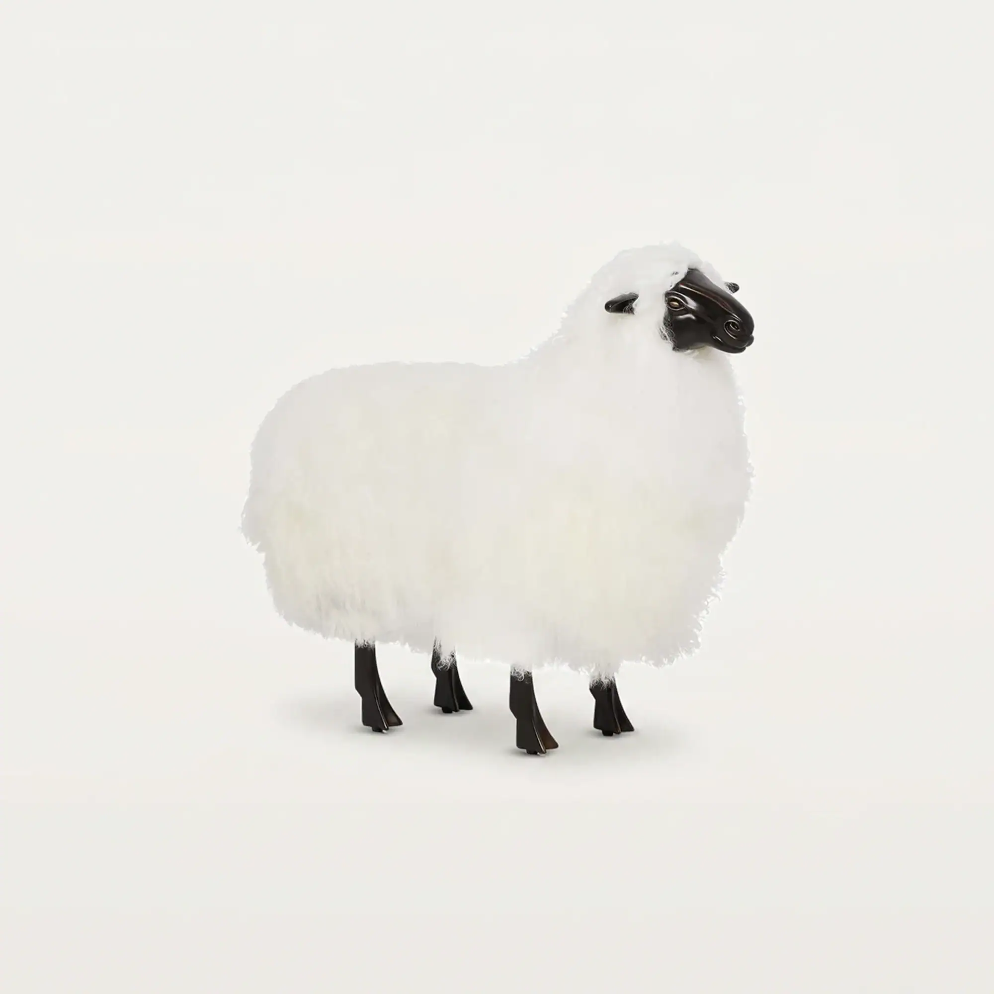 A white fluffy sheep figurine with a dark brown head and legs, standing on a light background.