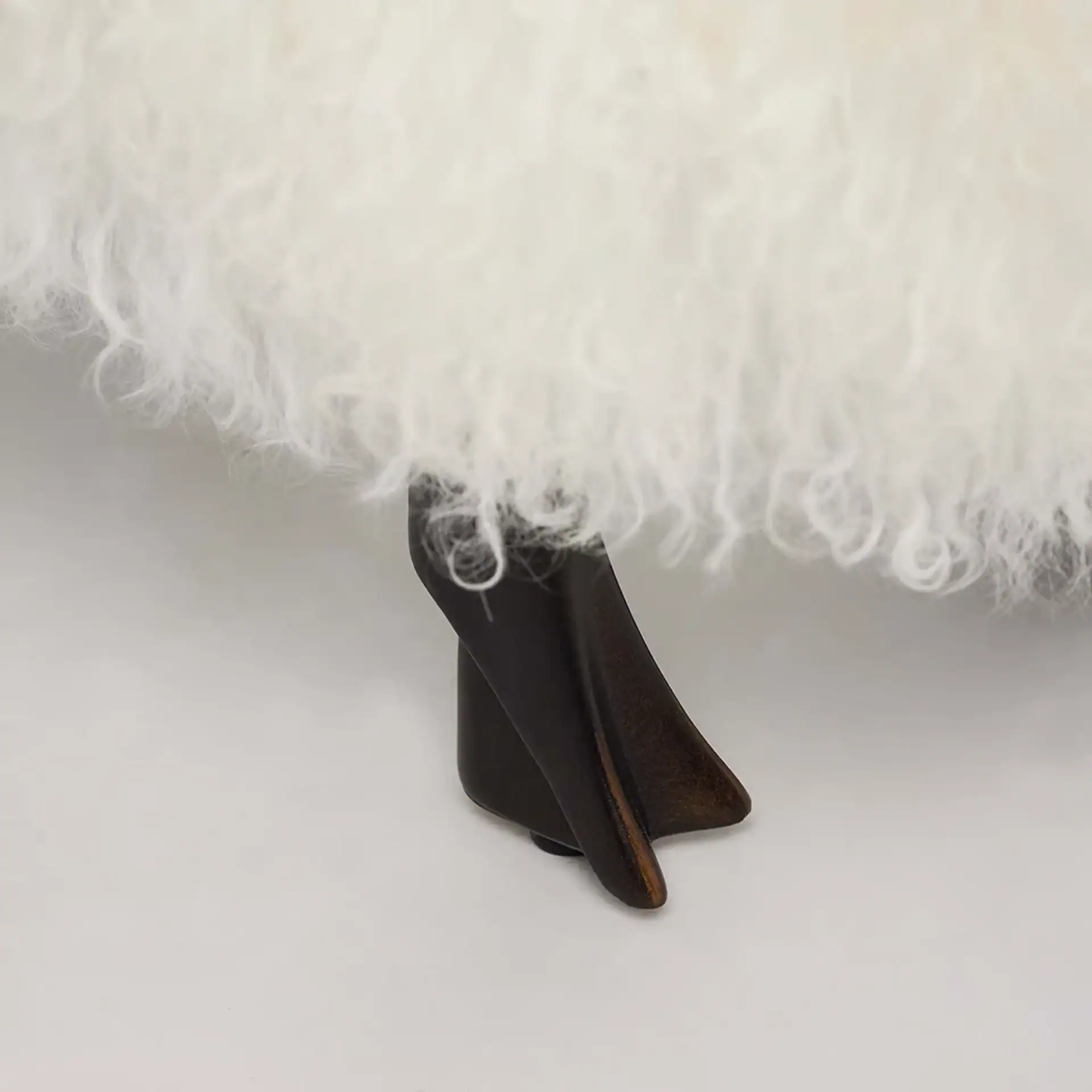 Close-up of a white fluffy texture above a dark, sculpted leg on a light grey background.