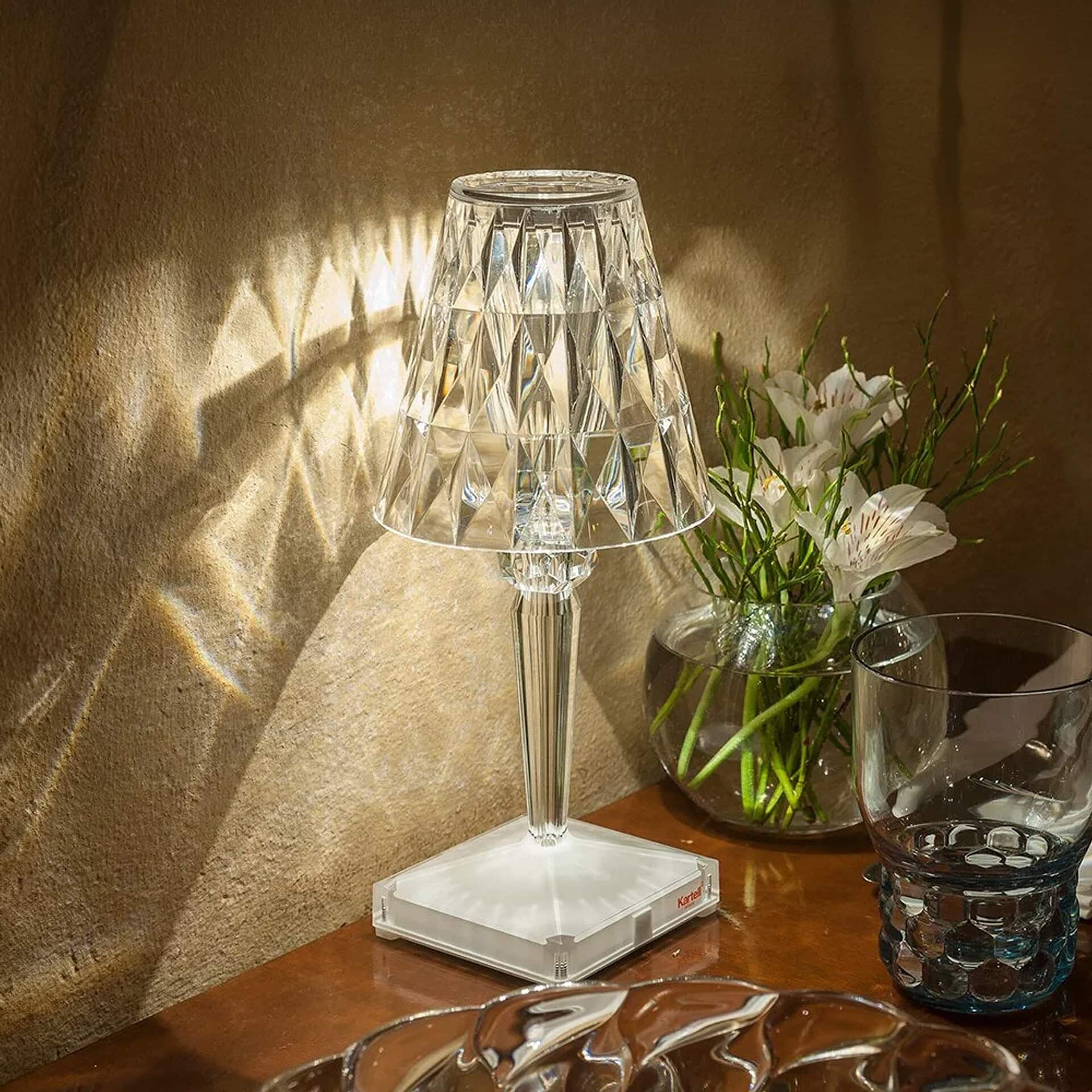 Elegant crystal table lamp with a decorative shade, paired with a glass vase of white flowers, on a.