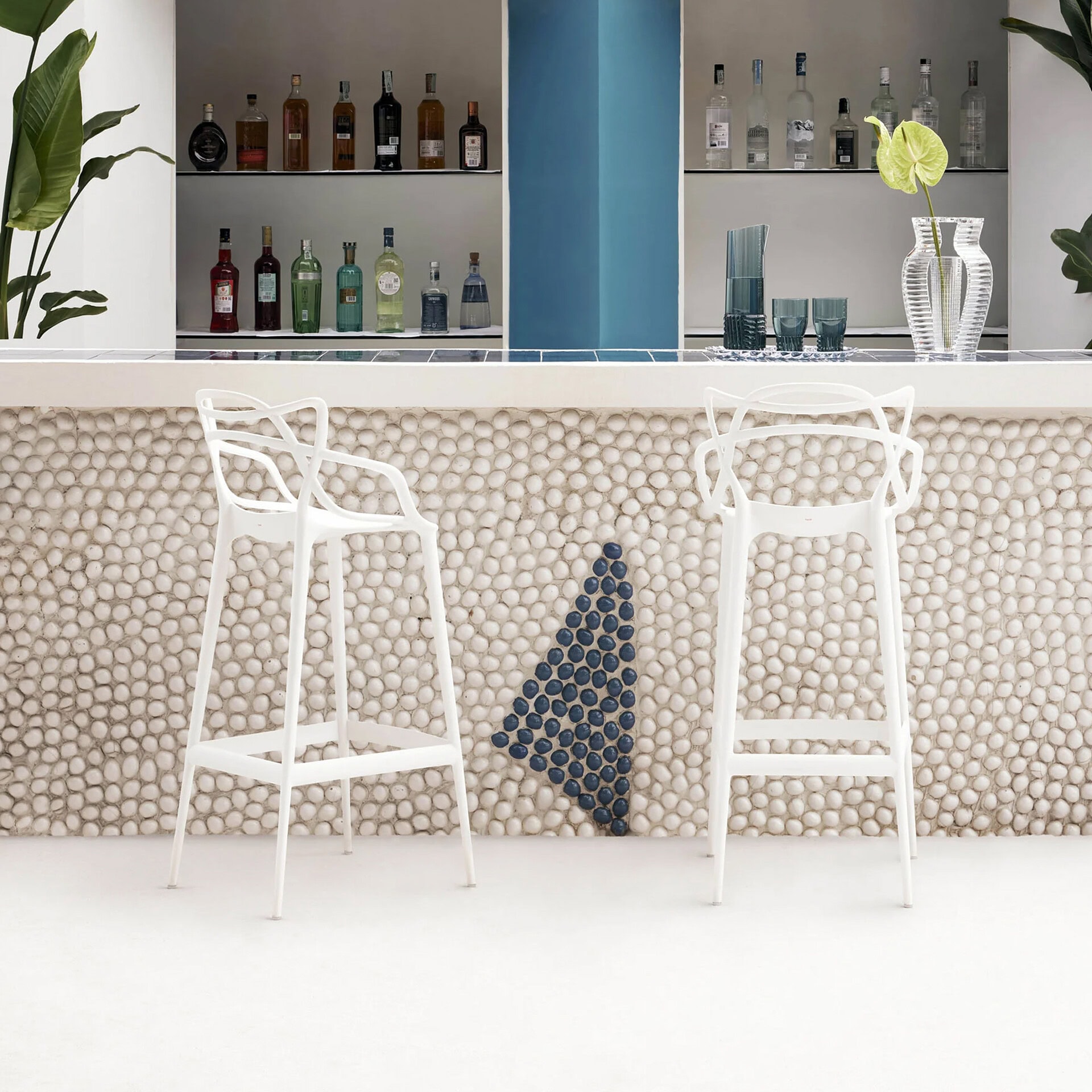 Contemporary bar with white stools, textured pebble wall, and colorful liquor bottles in the backgro.