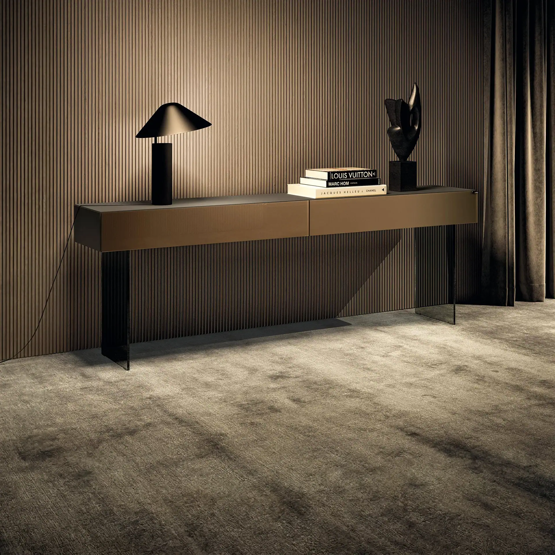 A modern console table with a black lamp, a stack of fashion books, and an abstract sculpture, set against a fluted wall with a dark curtain and plush carpet.